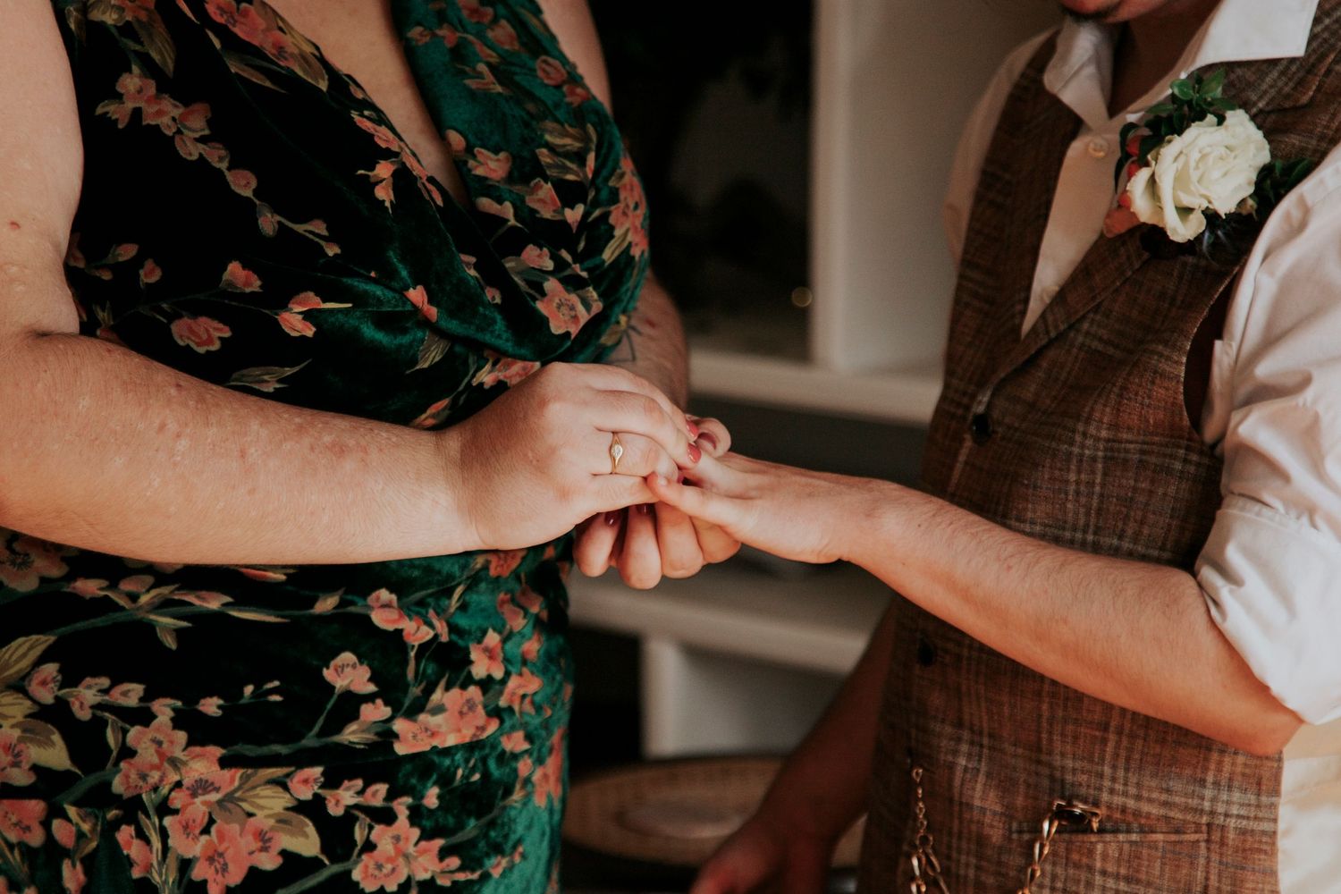 Two hands hold each other tenderly during a romantic engagement photo session with floral dress and brown vest.