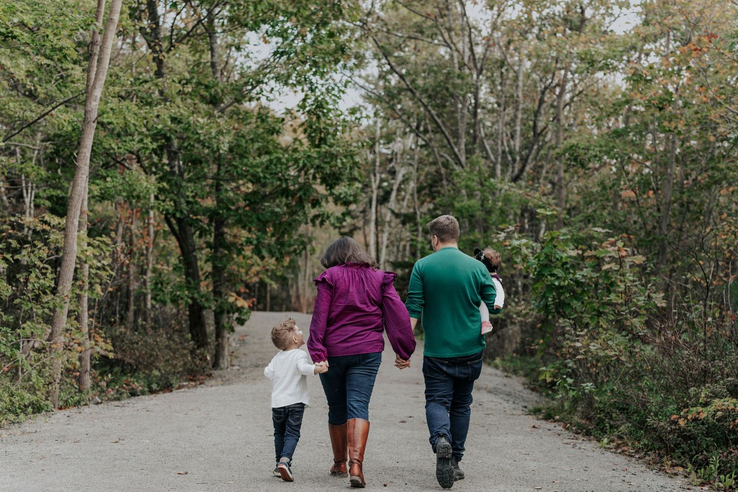 Family of four walking hand-in-hand down a tree-lined path in autumn.