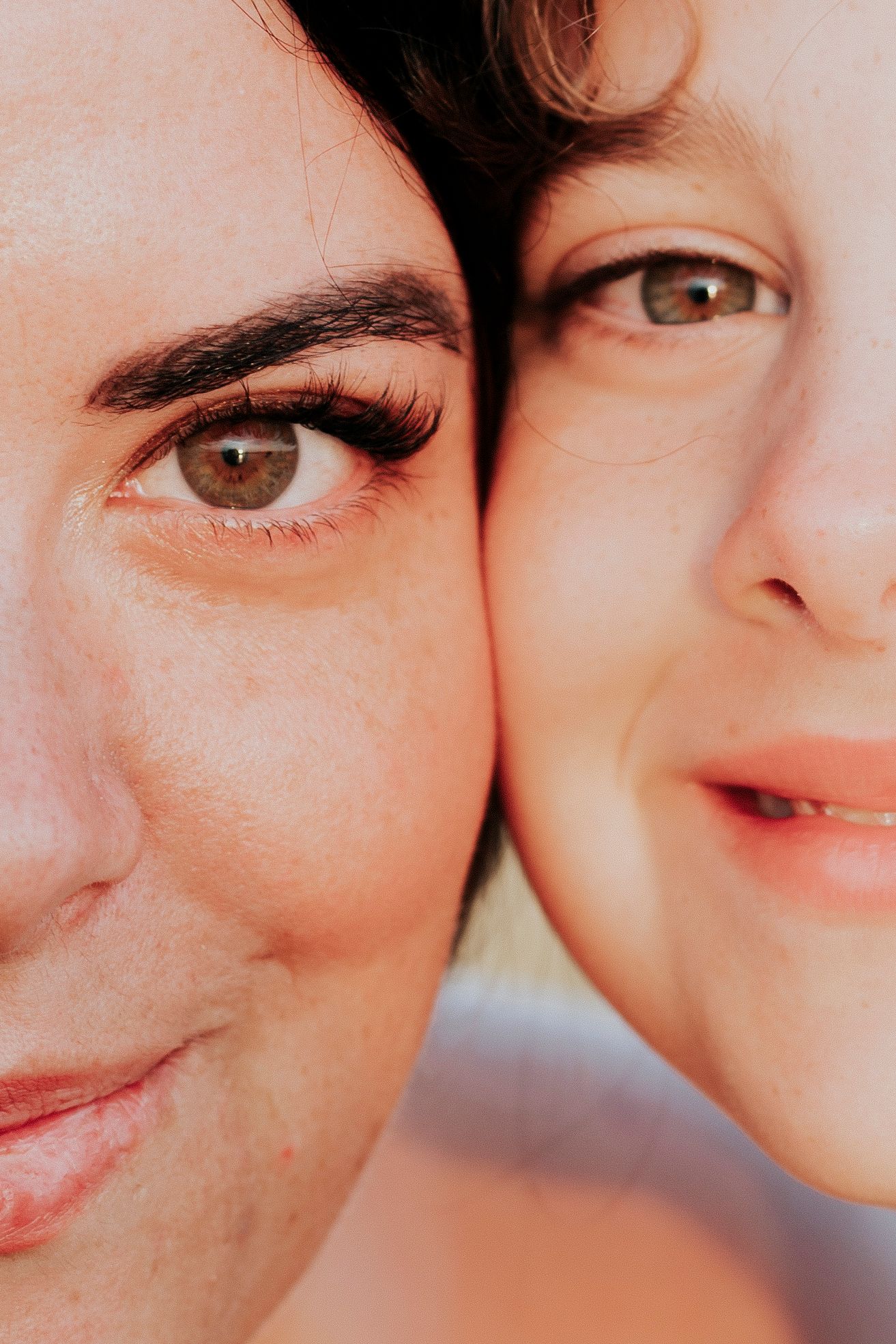 Close-up portrait of two women with brown eyes pressing their faces together cheek to cheek.