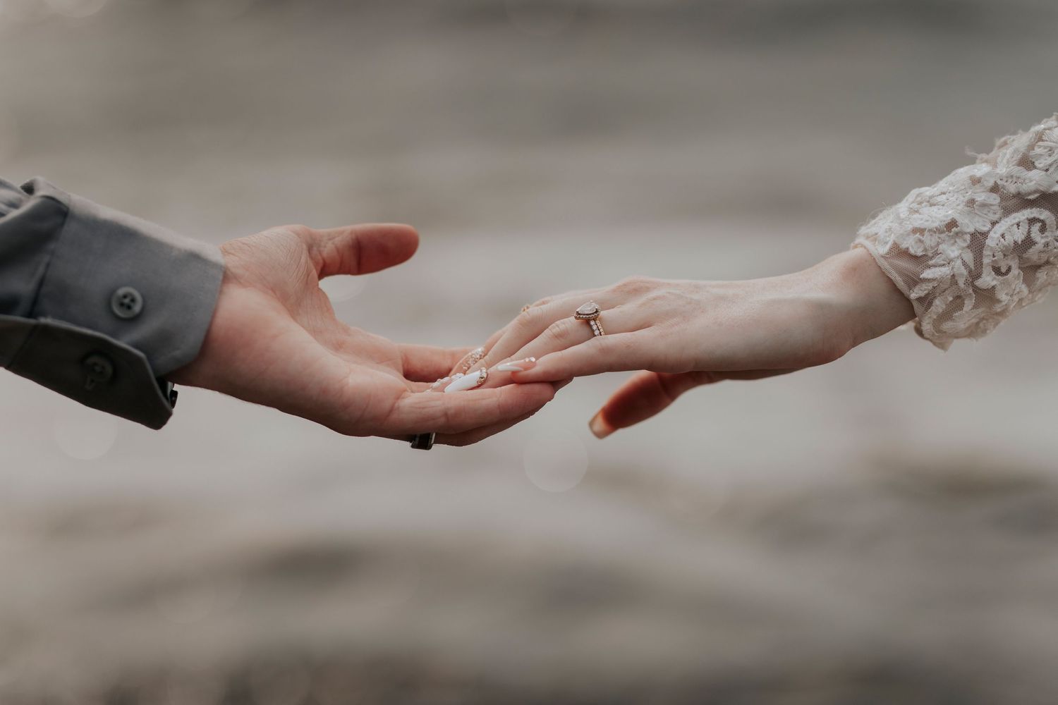 Bride and groom gently reaching toward each other with hands touching, showcasing an engagement ring.