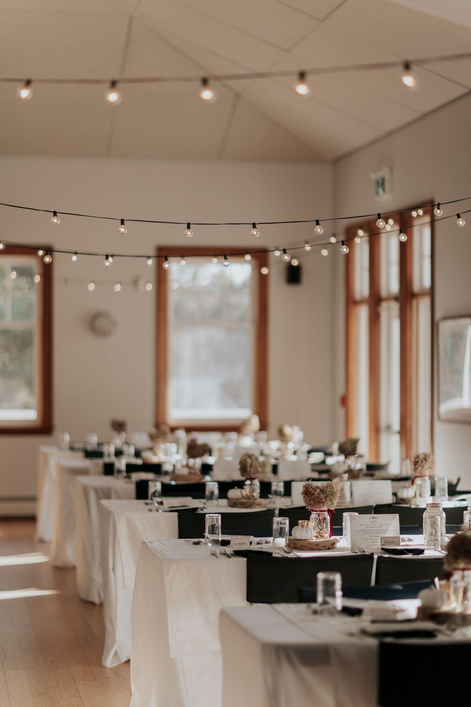 Wedding reception venue with elegant table settings and string lights hung from wooden beam ceiling.