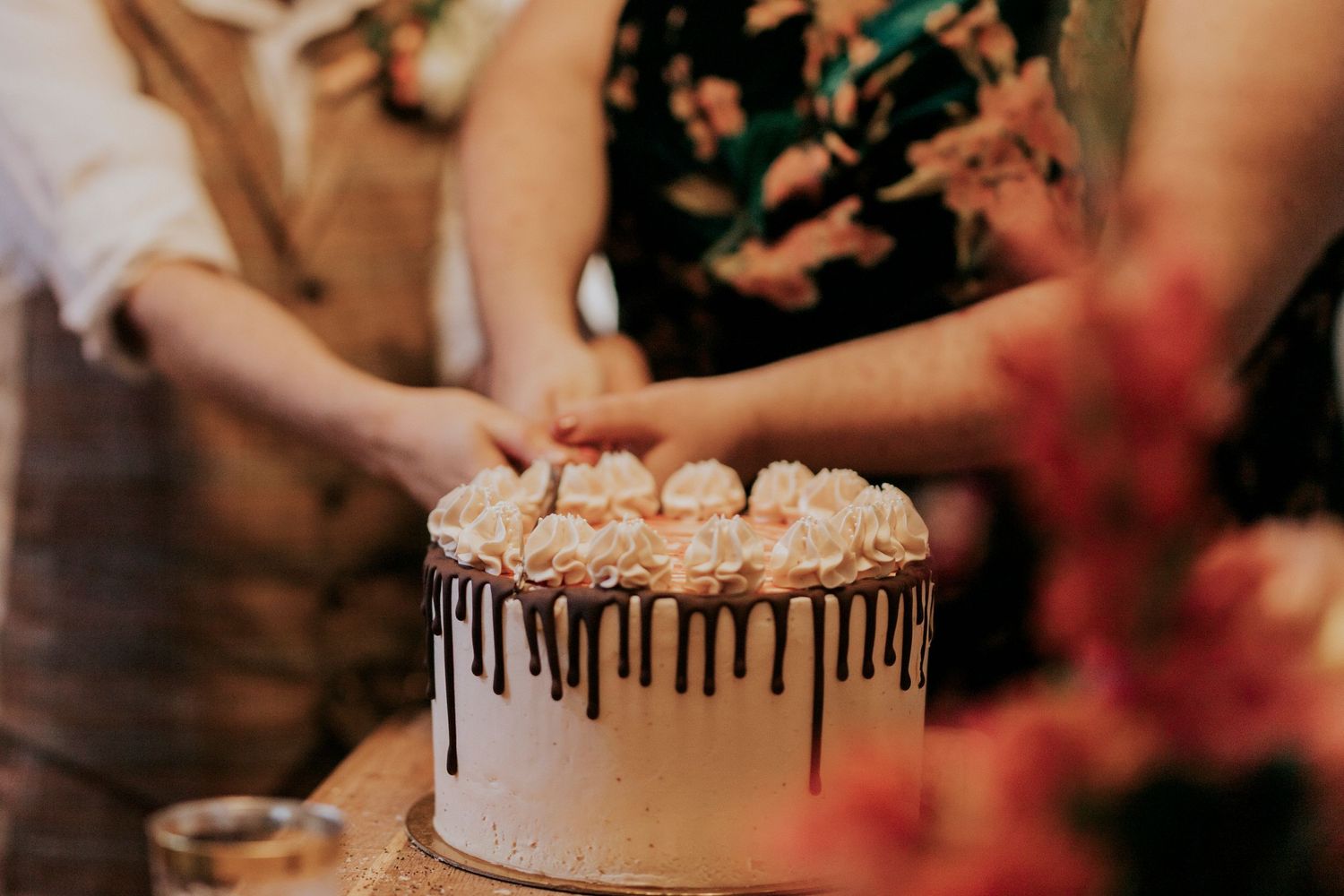 Hands reaching for an elegant white drip cake at a celebration.