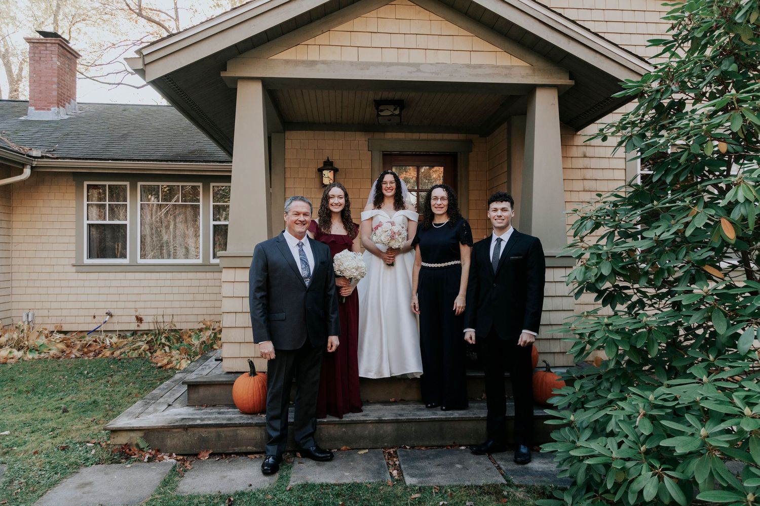 A small group gathers on the front porch of a craftsman style house with autumn decorations.