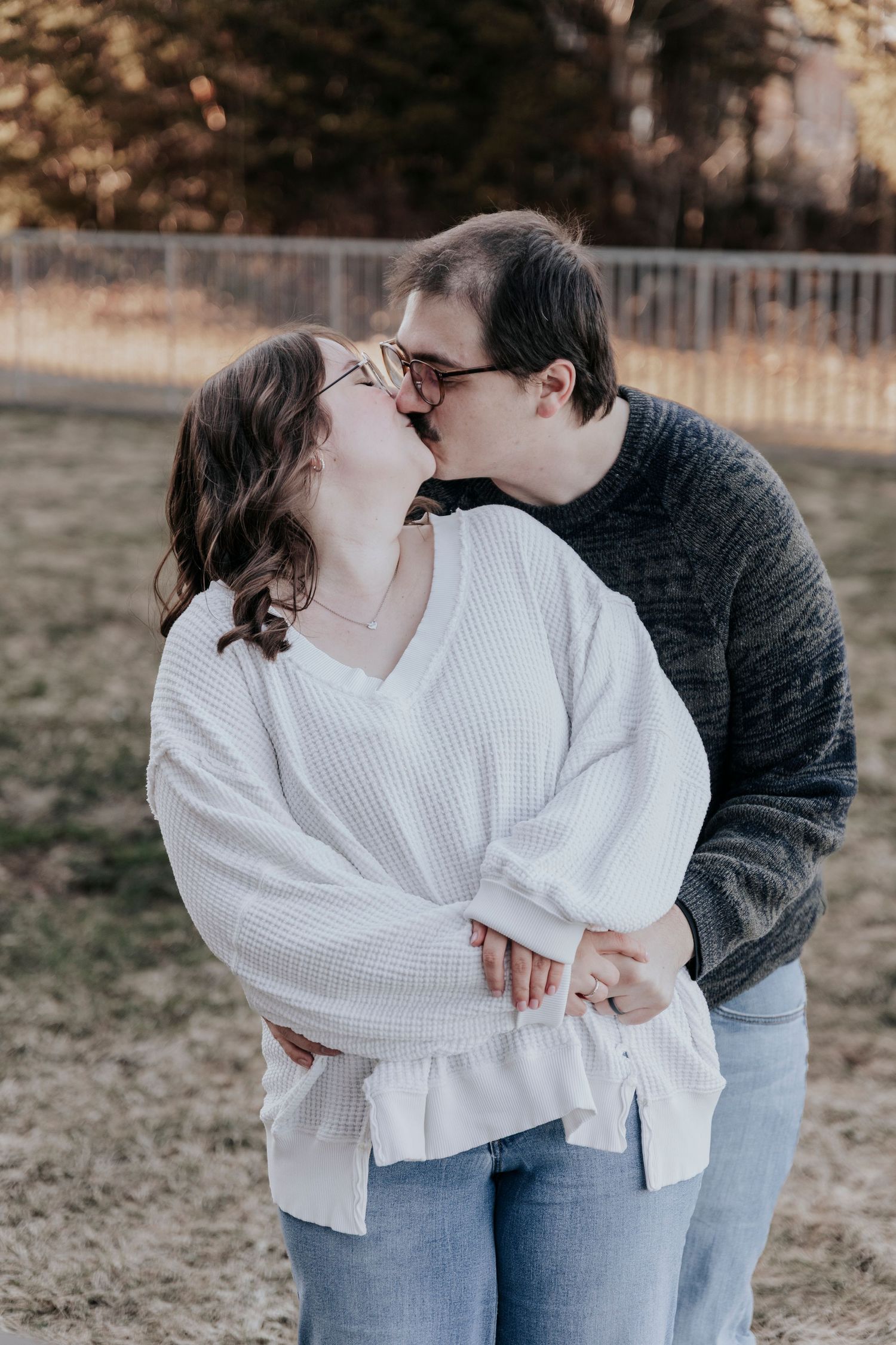 Couple sharing a tender kiss outdoors in a sunlit park during autumn season.