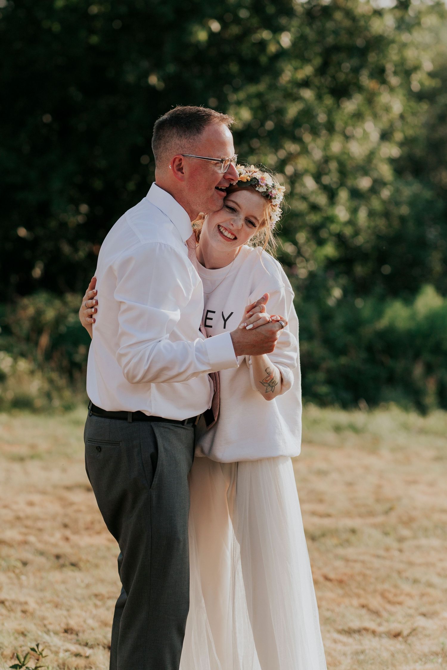 A heartwarming embrace between father and daughter at an outdoor wedding, with soft sunlight and natural greenery in the background.