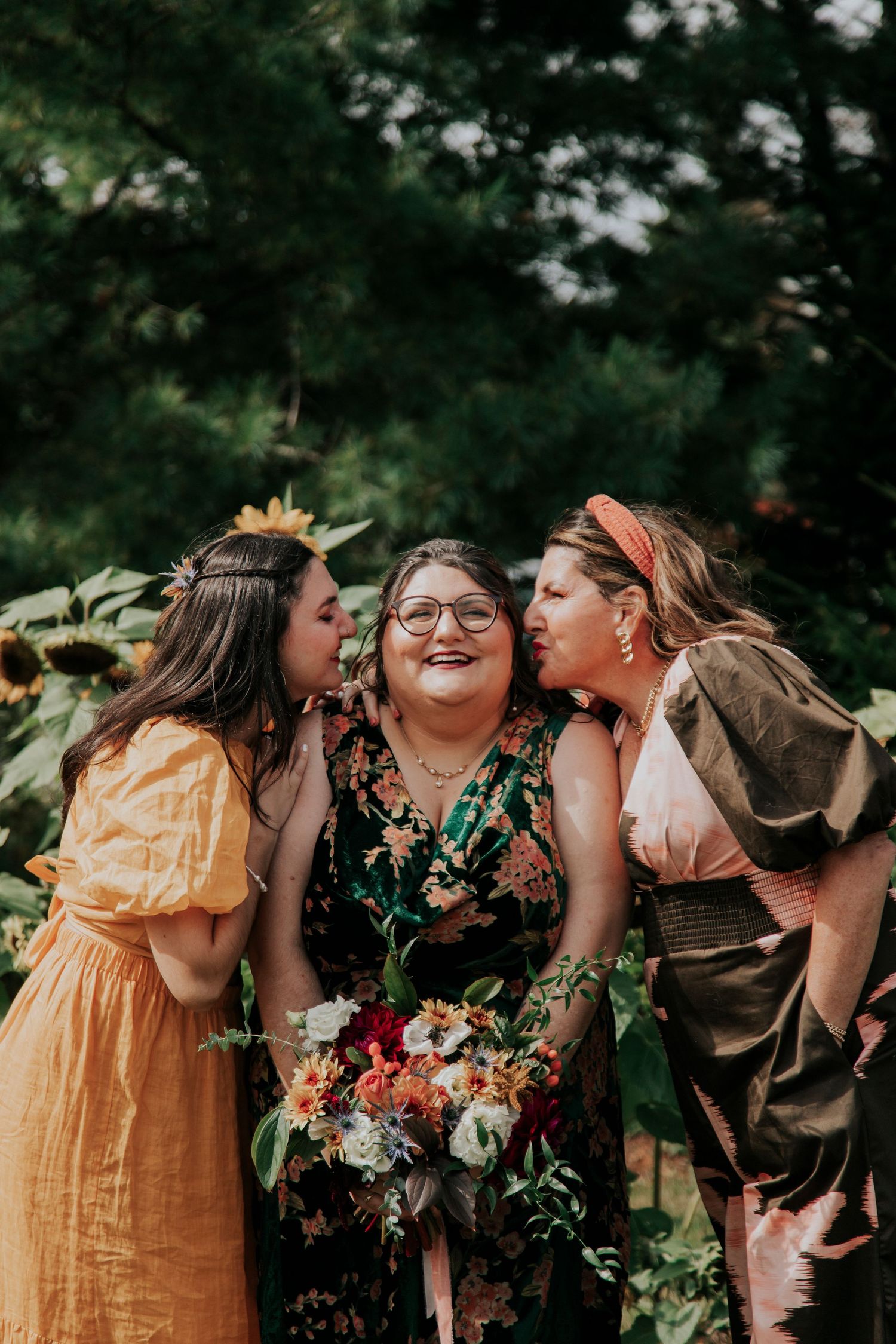 Three people sharing a joyful moment together while holding a beautiful autumn-themed floral bouquet in an outdoor setting.