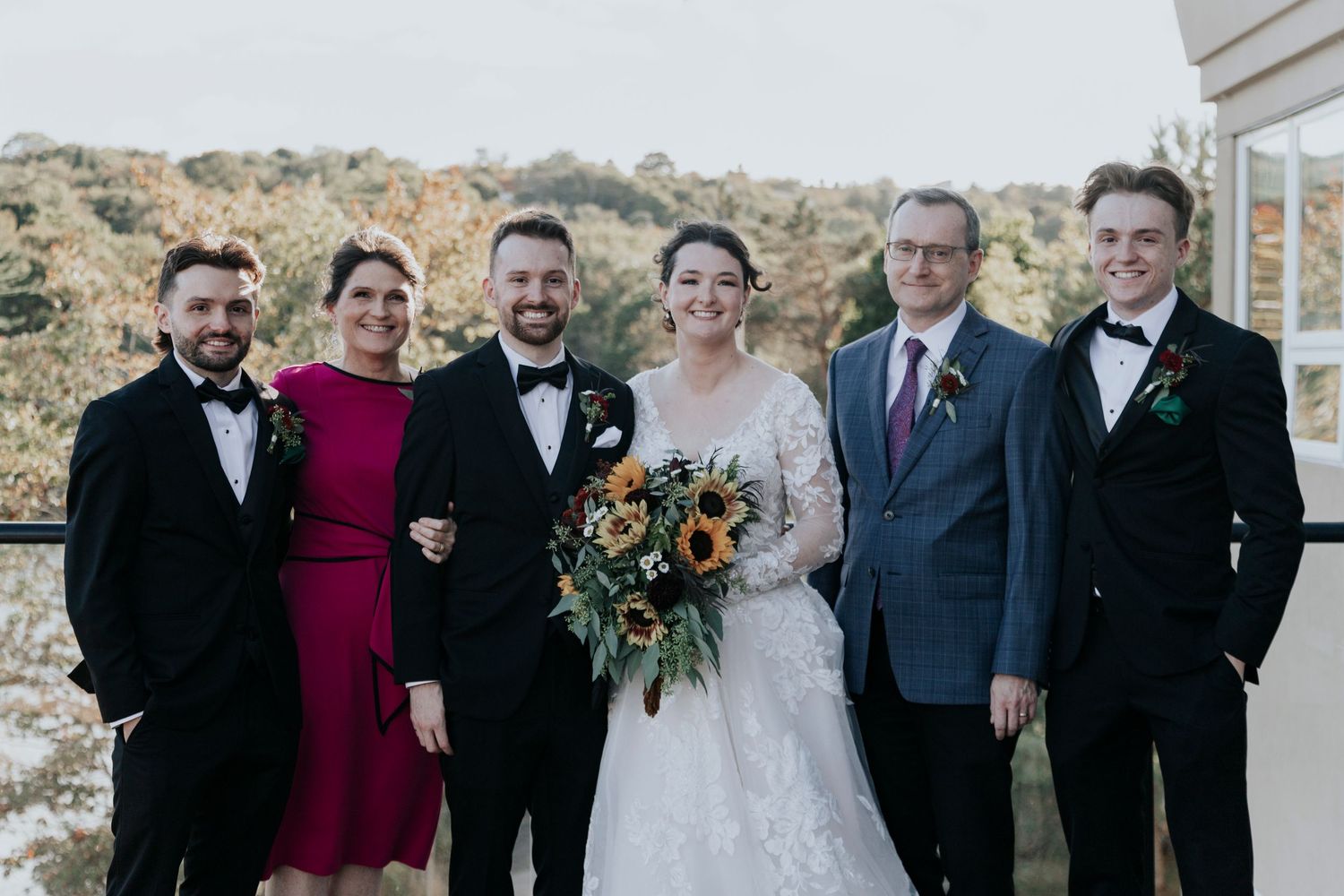 Wedding party poses together on a balcony with a bright fall landscape behind them.