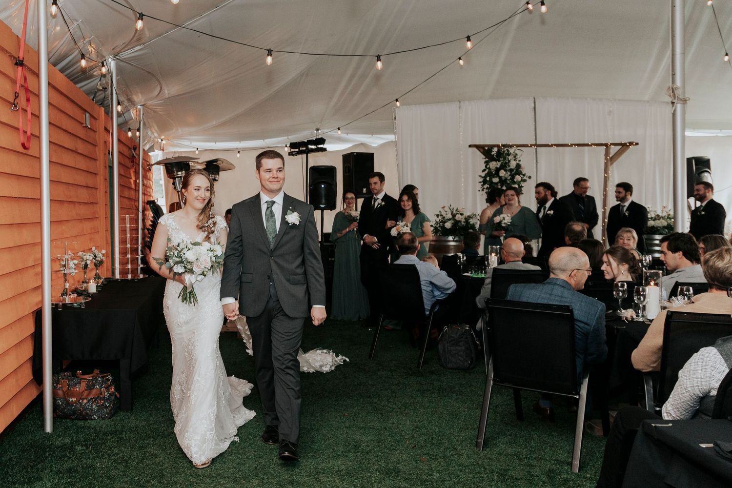 Wedding reception in a tent with string lights and guests seated at tables.