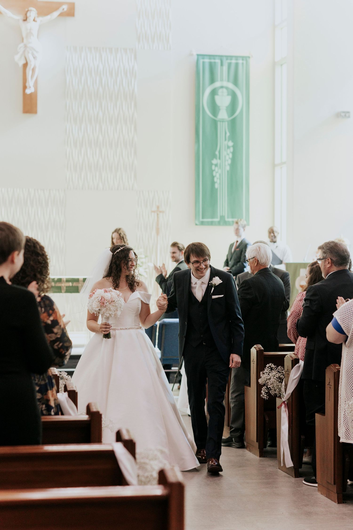 A couple walks down the aisle of a church during their wedding ceremony with guests seated in wooden pews.