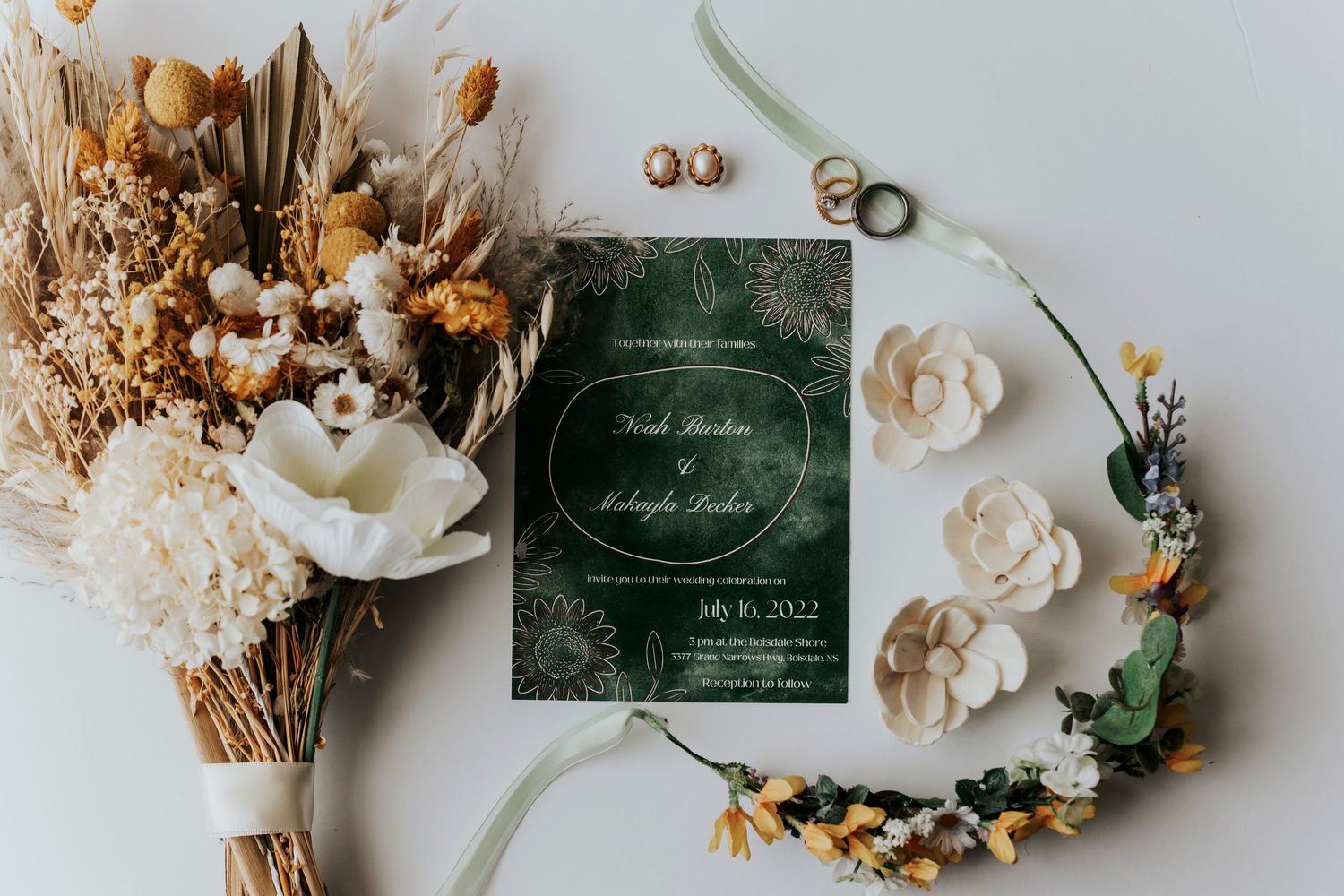 Elegant dark green wedding invitation with dried flower bouquets and white roses arranged on white background.