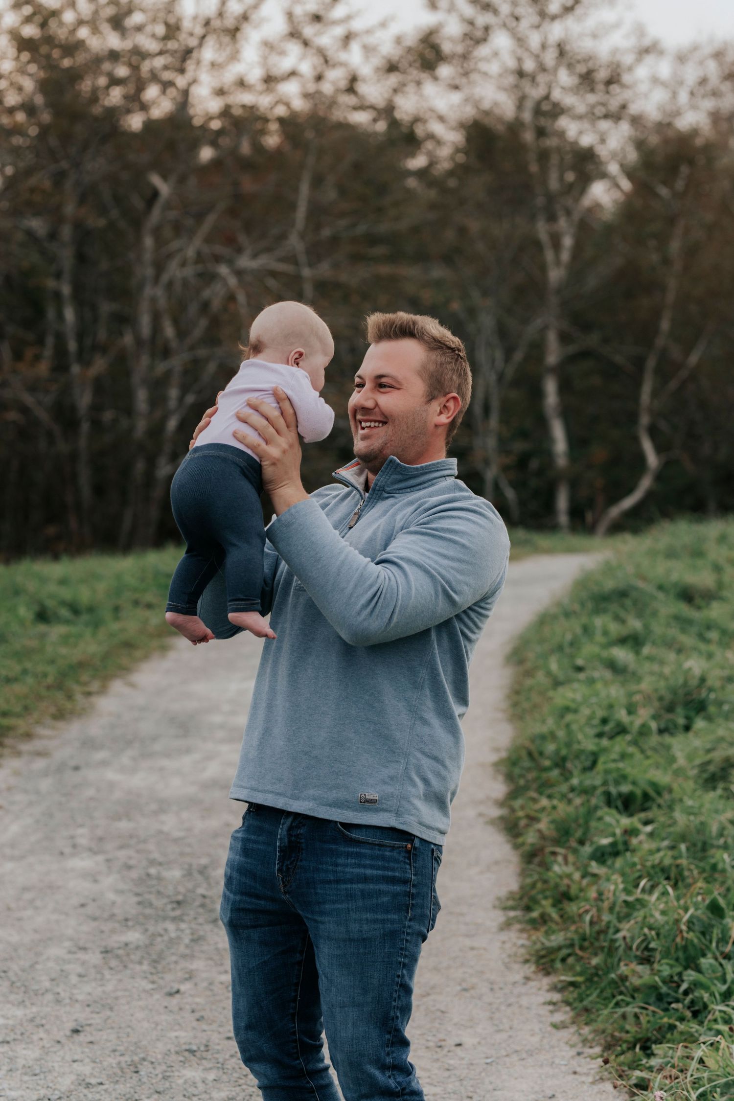 Joyful father lifting laughing baby on scenic outdoor pathway.