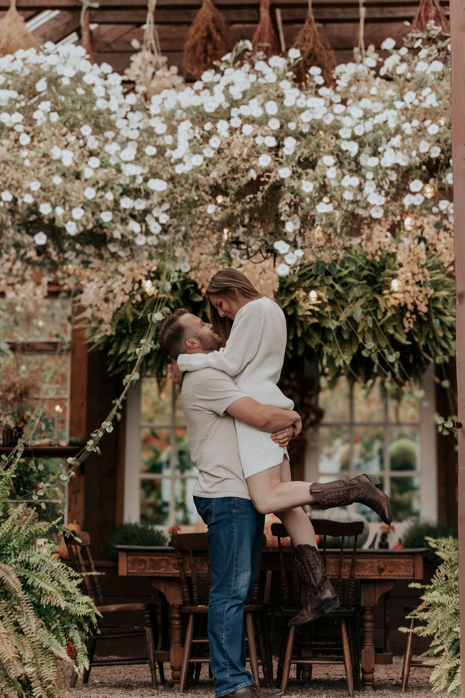 Man lifting woman in a joyful embrace beneath a stunning floral ceiling installation.