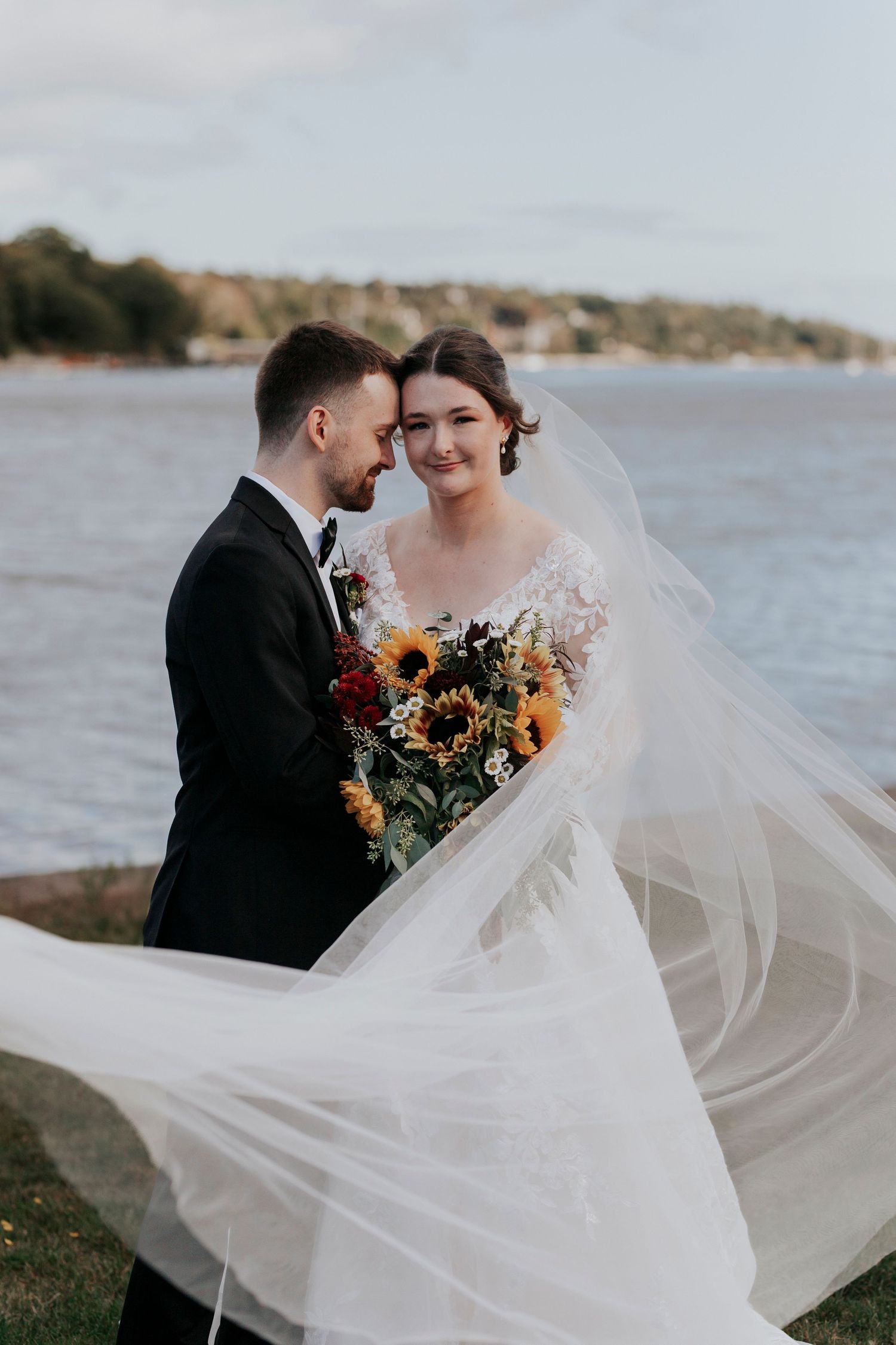Waterfront wedding portrait with billowing veil and sunflower bouquet.