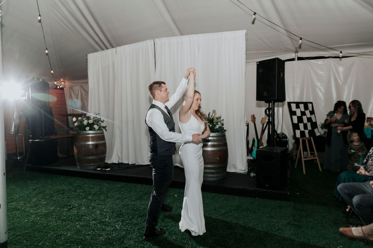 Couple shares their first dance at reception in white tent with wine barrels and artificial grass floor.