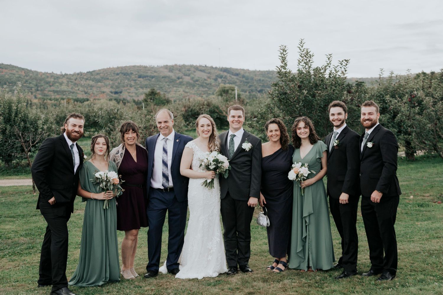 Wedding party group photo outdoors with mountain landscape in background.