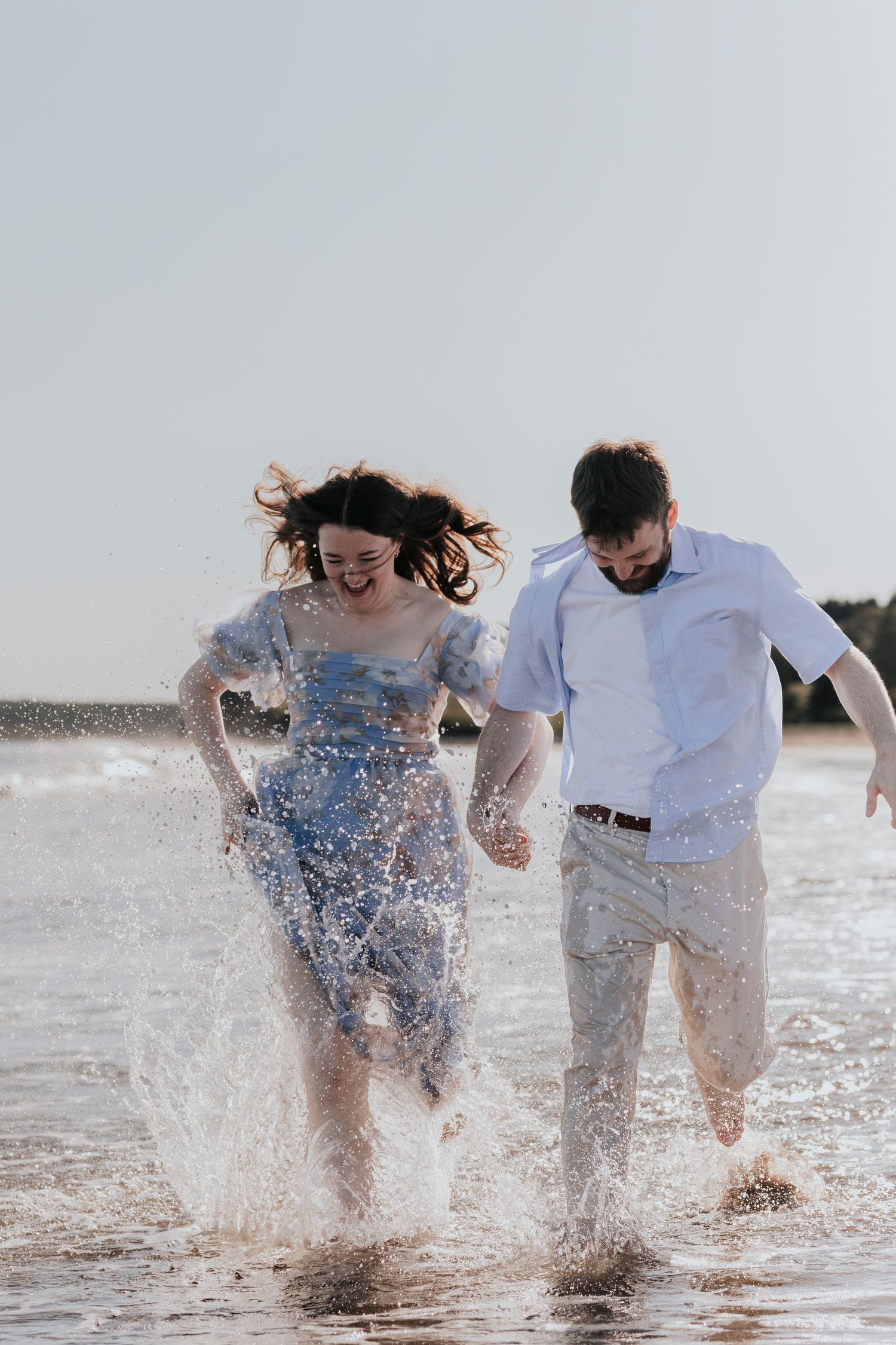 Happy couple running and splashing through ocean waves on a sunny beach, laughing together.