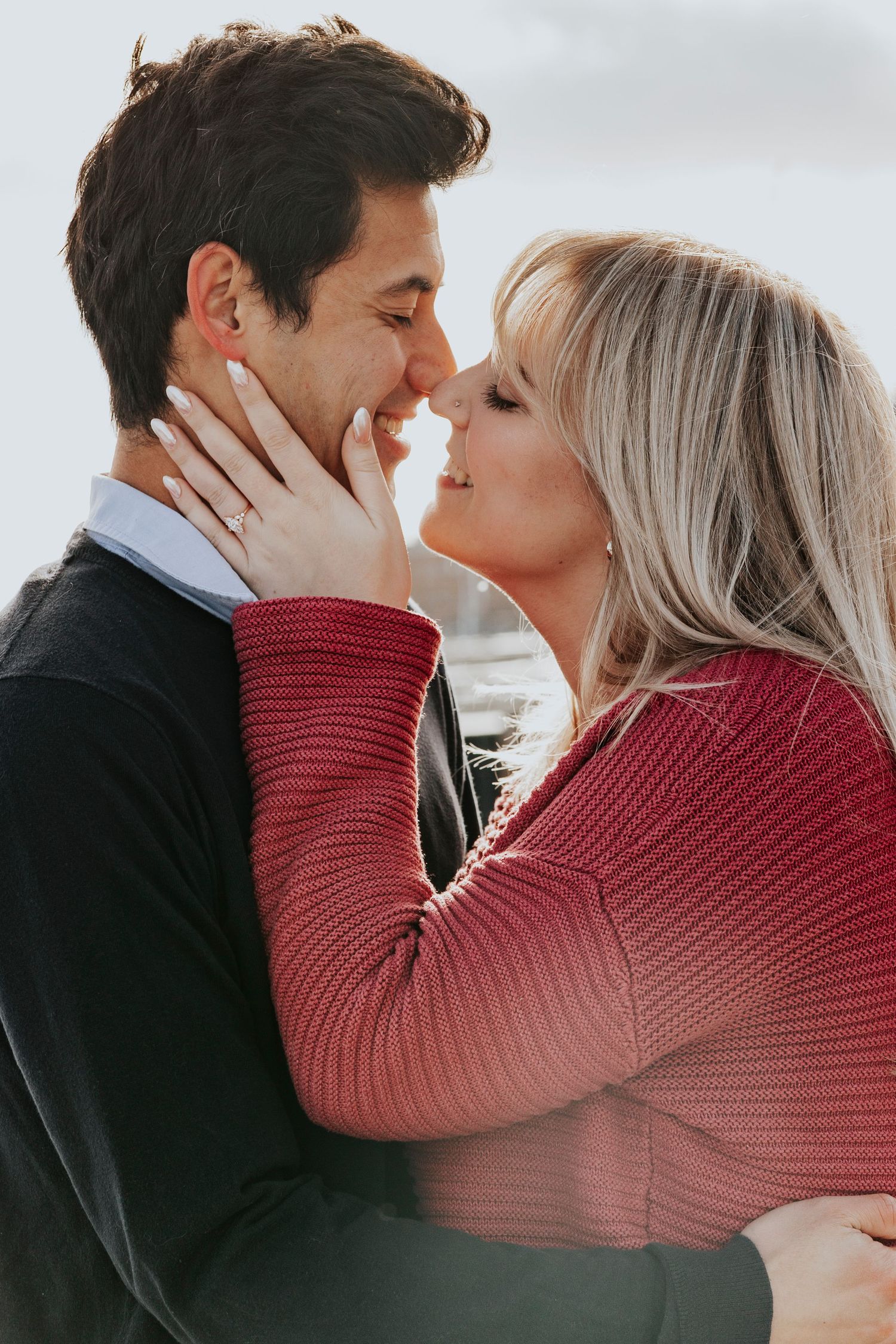 Engaged couple sharing a close romantic moment, woman showing diamond ring while embracing outdoors.