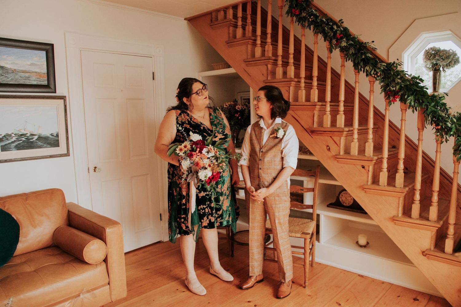 A candid moment between a bride and groom in a warm living room with a wooden staircase adorned with garland.