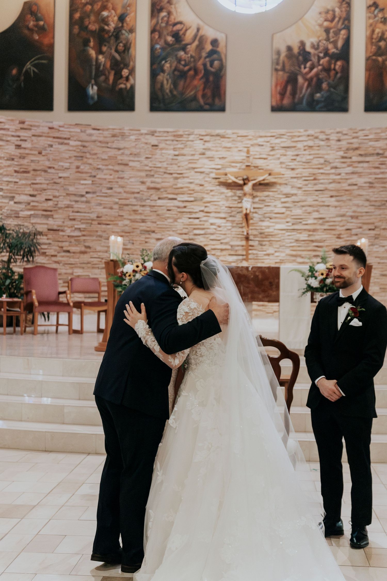 A wedding ceremony moment in a church with religious artwork and stone walls in the background.