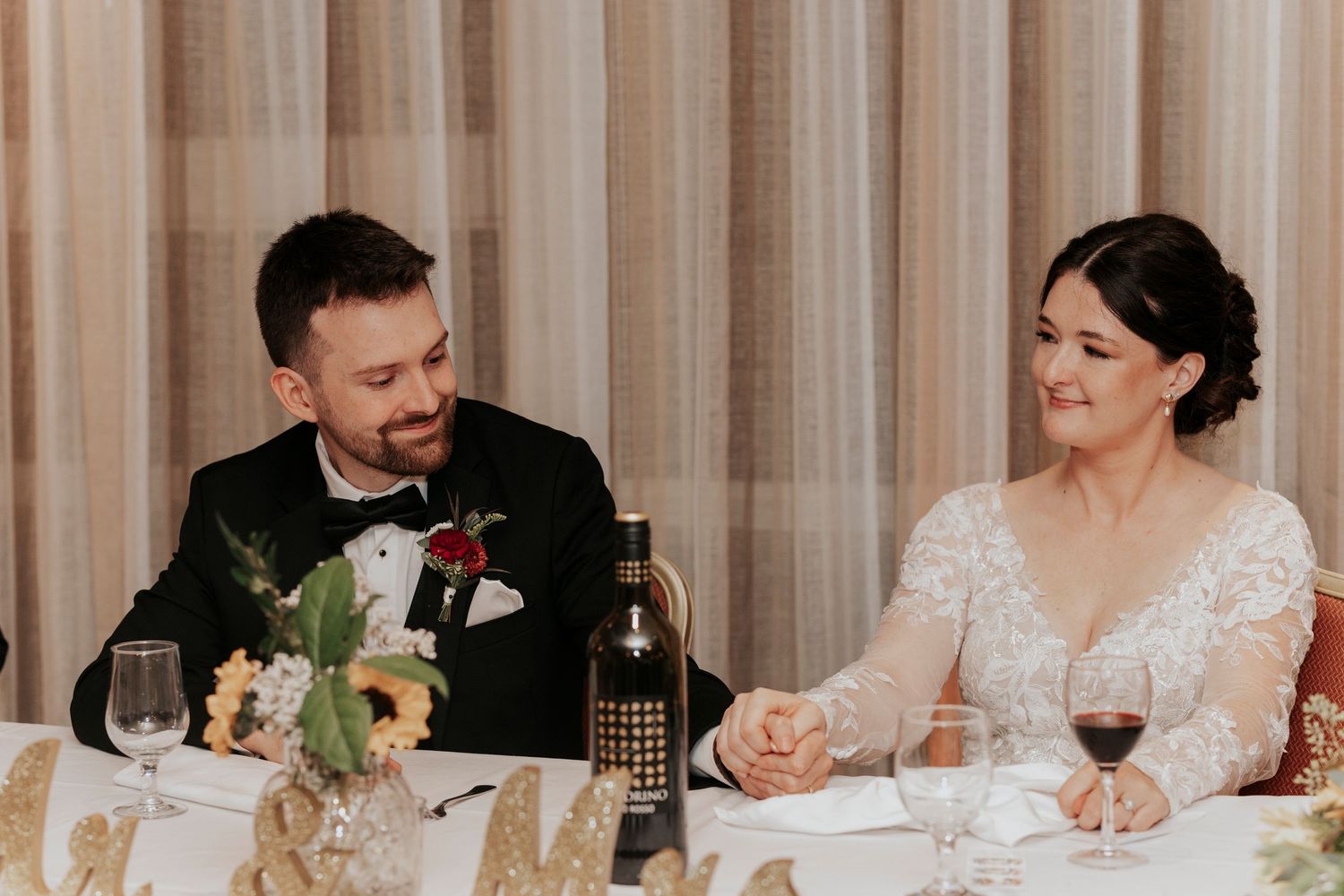 Newlywed couple shares a joyful moment while seated at their reception dinner table.
