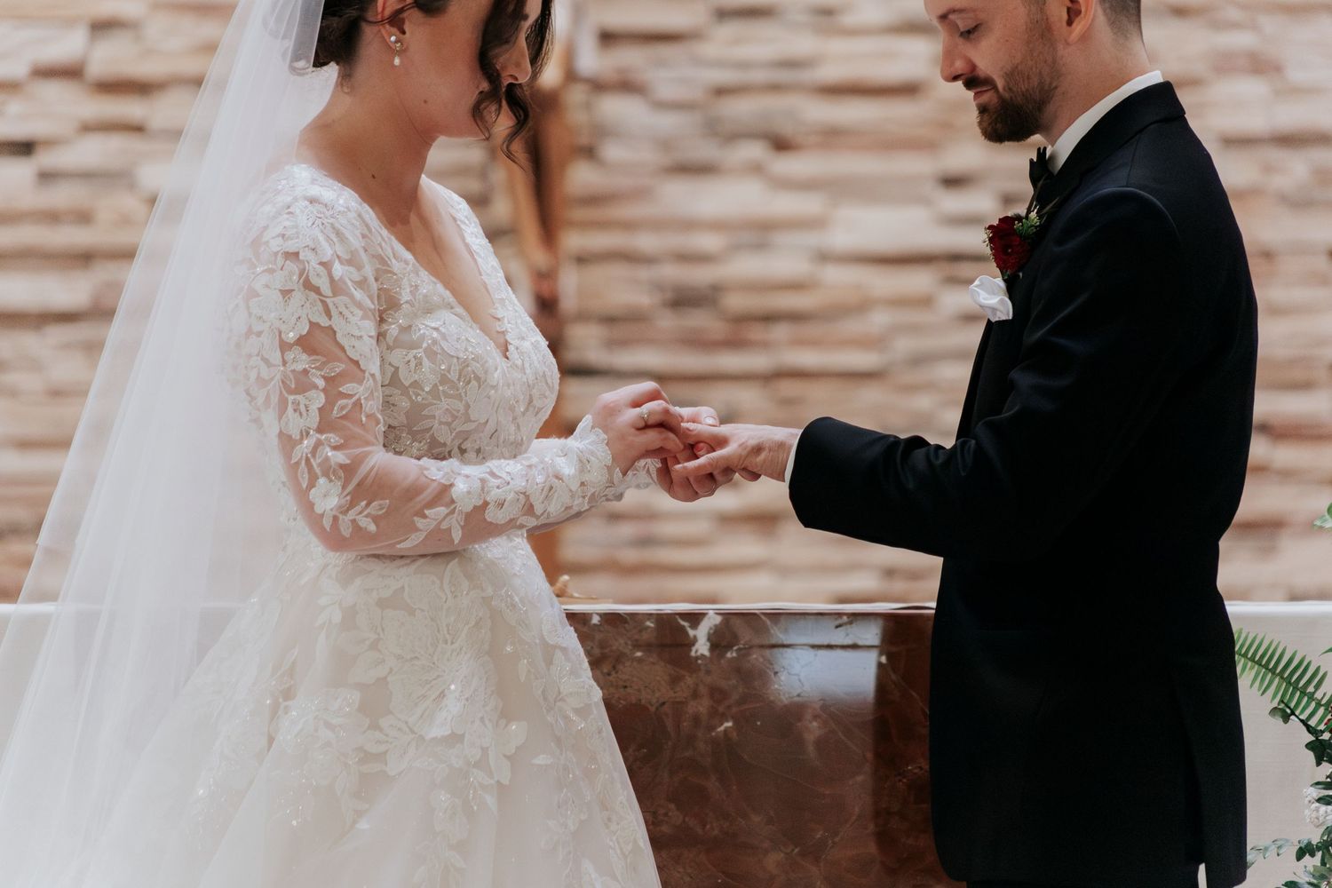 Exchanging wedding rings during ceremony in front of stone altar wall.