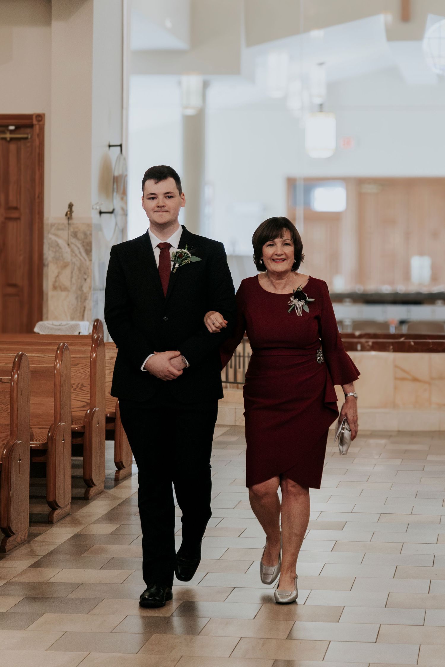 A formal couple walks down a church aisle during a wedding ceremony.