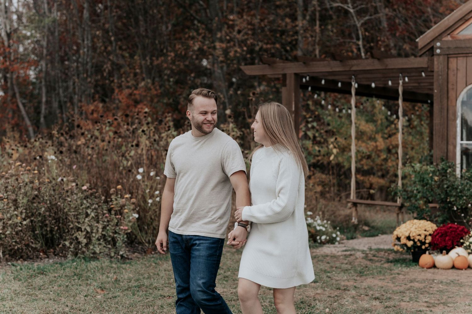 Young couple holding hands and smiling outdoors in autumn setting with fall decorations.