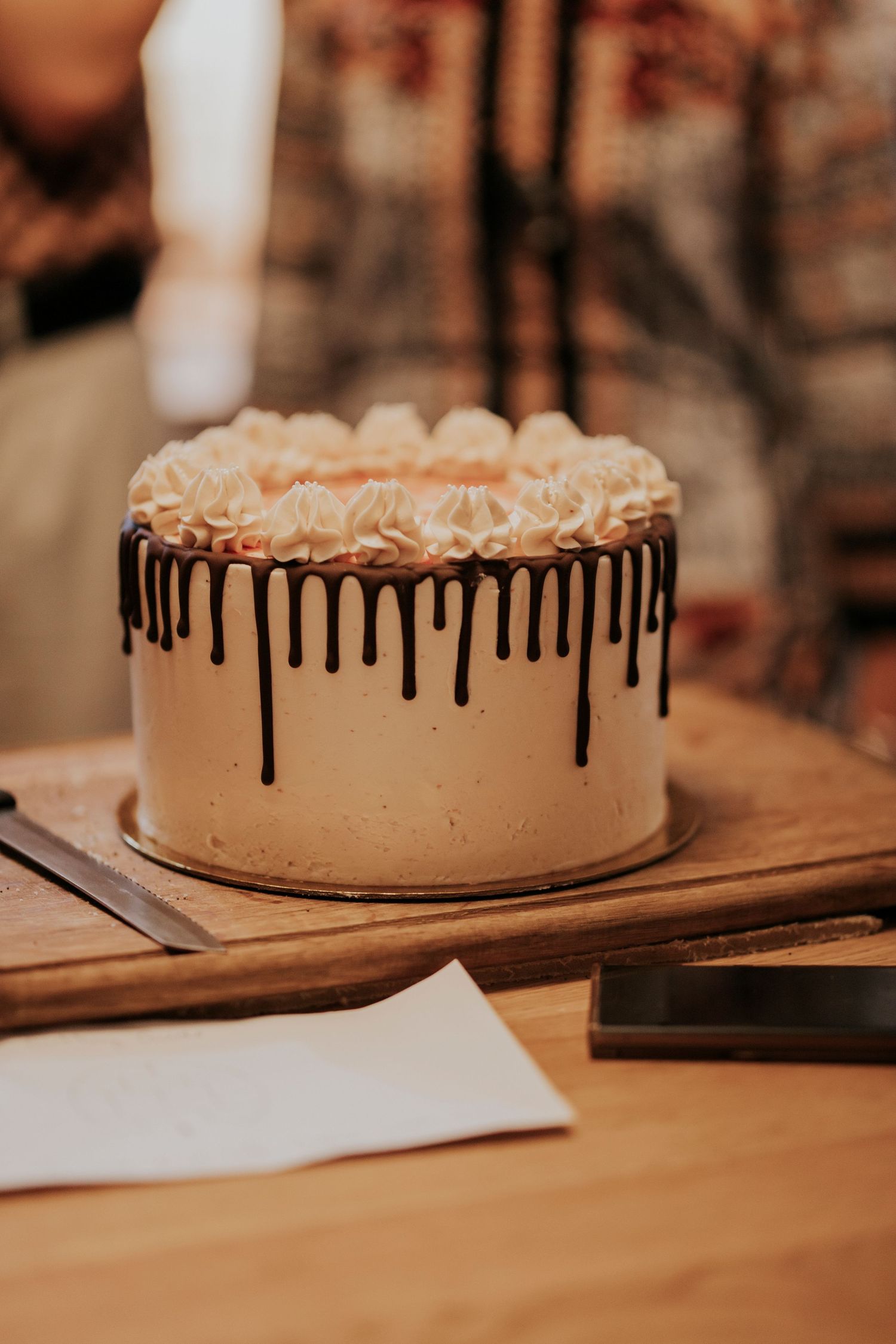 Elegant white cake with chocolate drip decoration and ruffled top on wooden serving board.