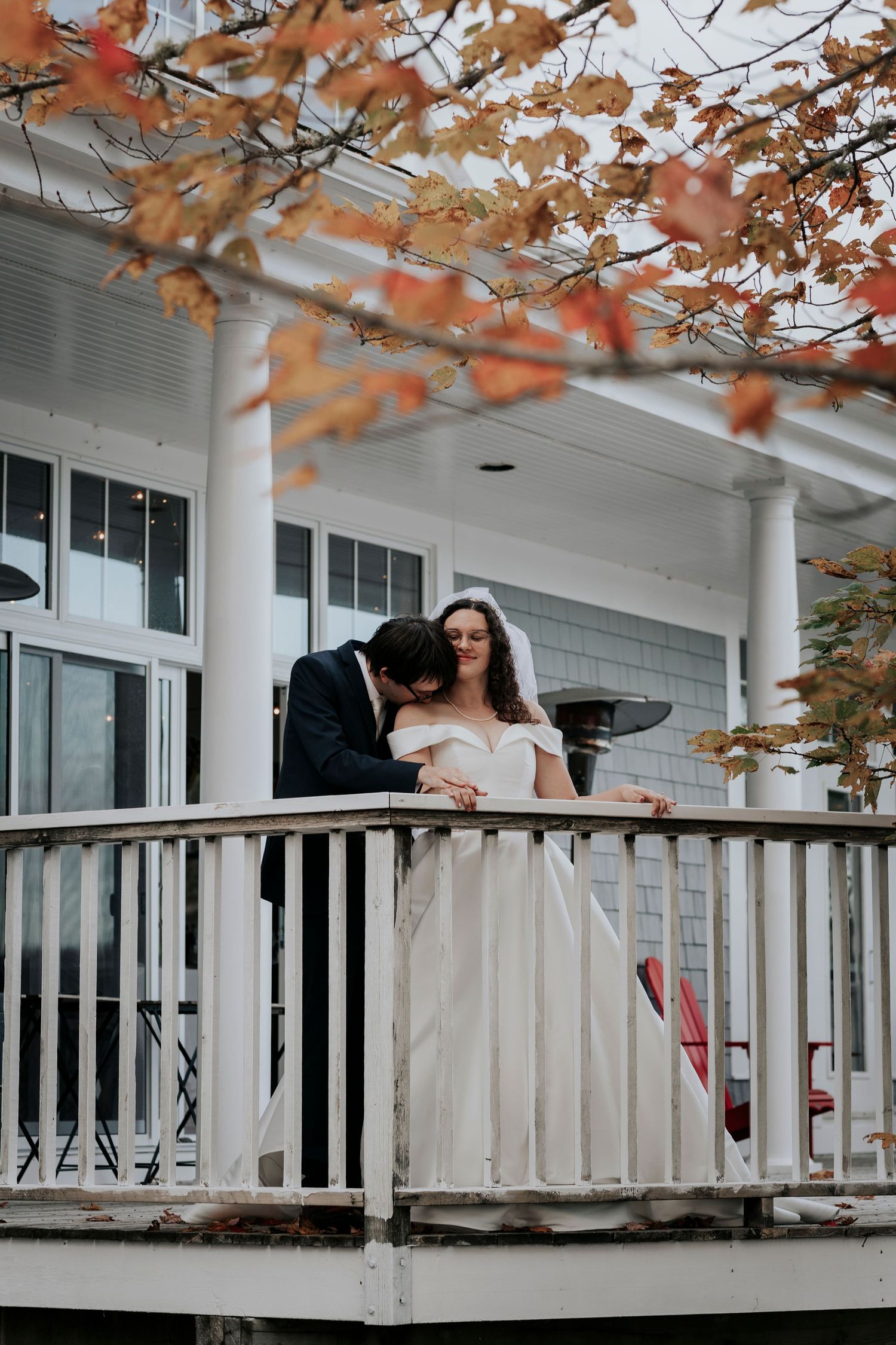 A white wedding dress worn on an autumn porch with orange fall foliage overhead and white columns visible.