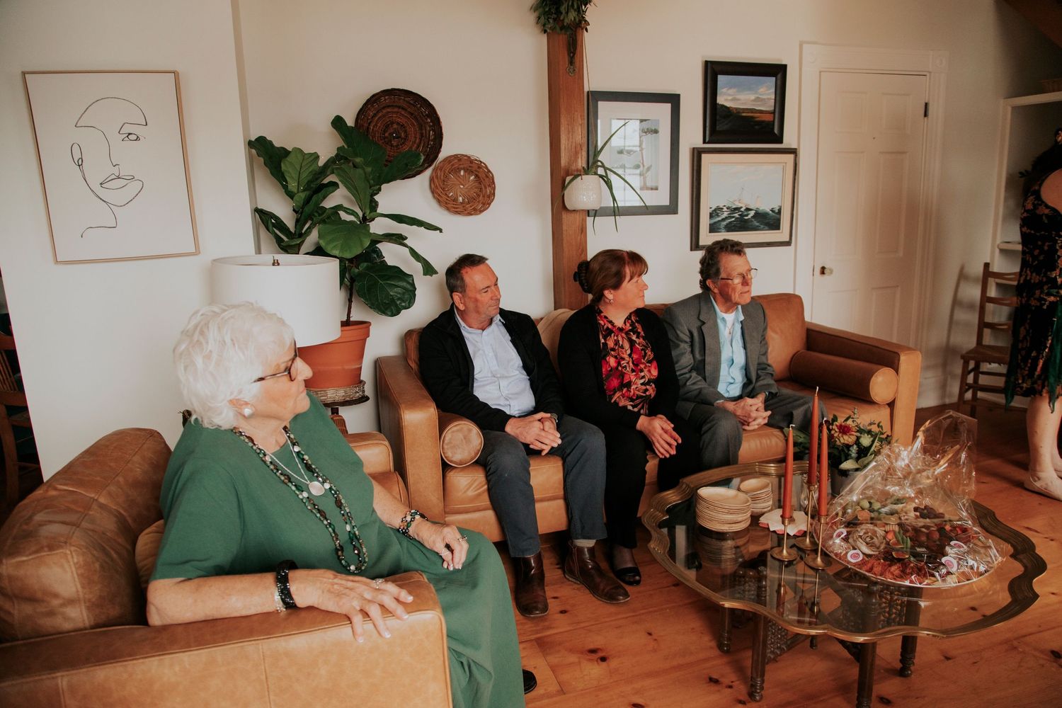 Four people sit and witness a wedding in a cozy living room decorated with wall art and indoor plants.