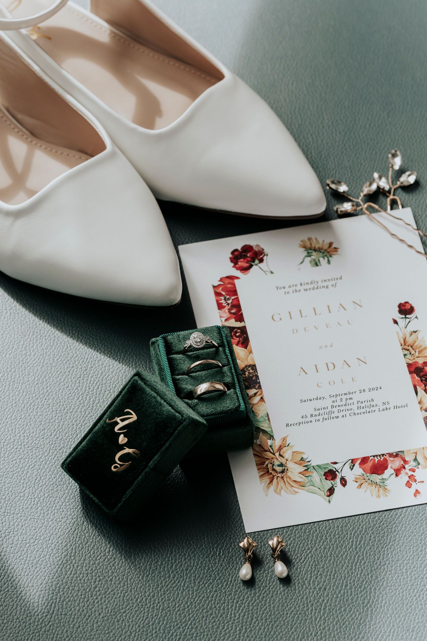 Wedding flat lay featuring white heels, green velvet ring box, invitation, and jewelry.