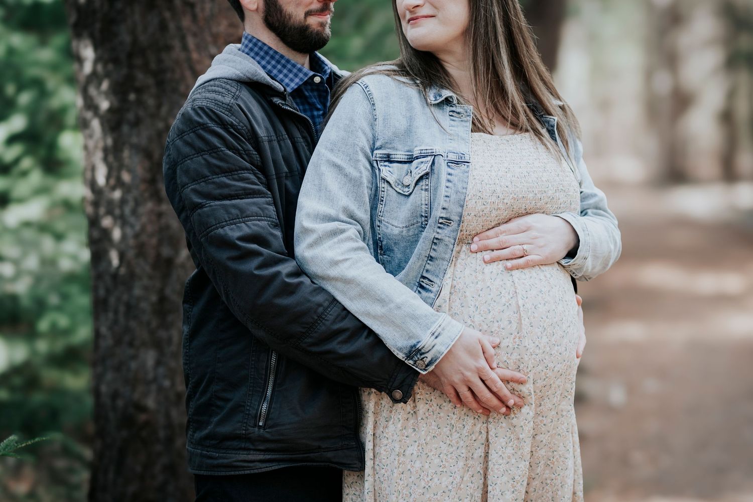 Expectant couple holding baby bump together in a serene forest during maternity photo session.