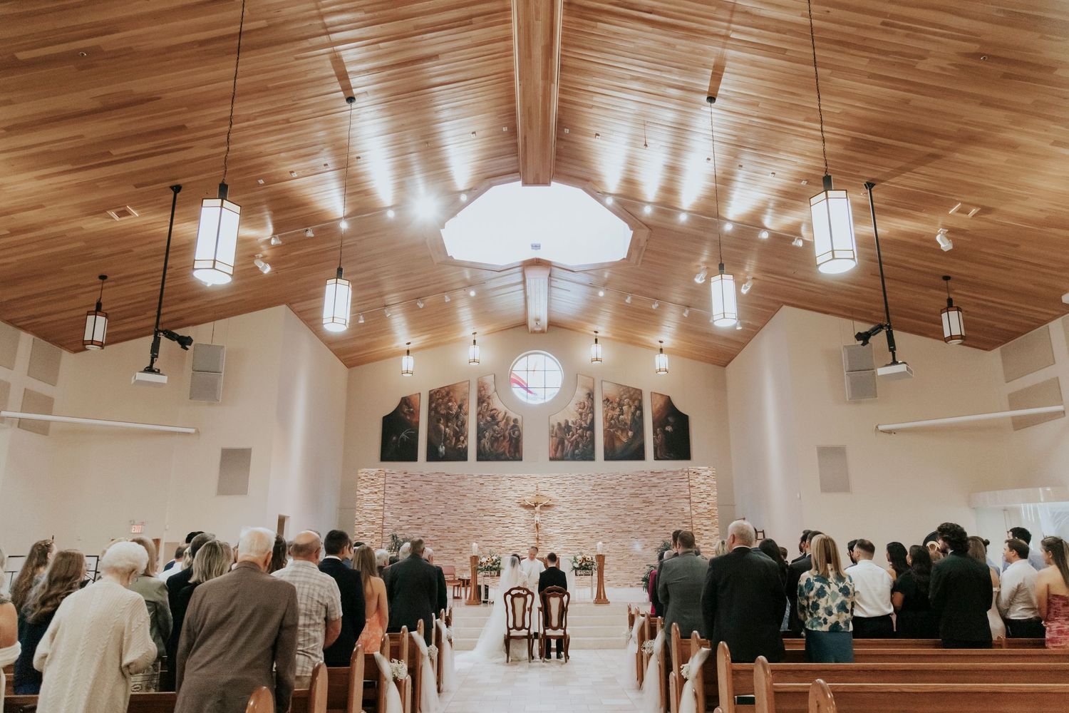 Wedding ceremony in a modern church with vaulted ceilings and hanging pendant lights.