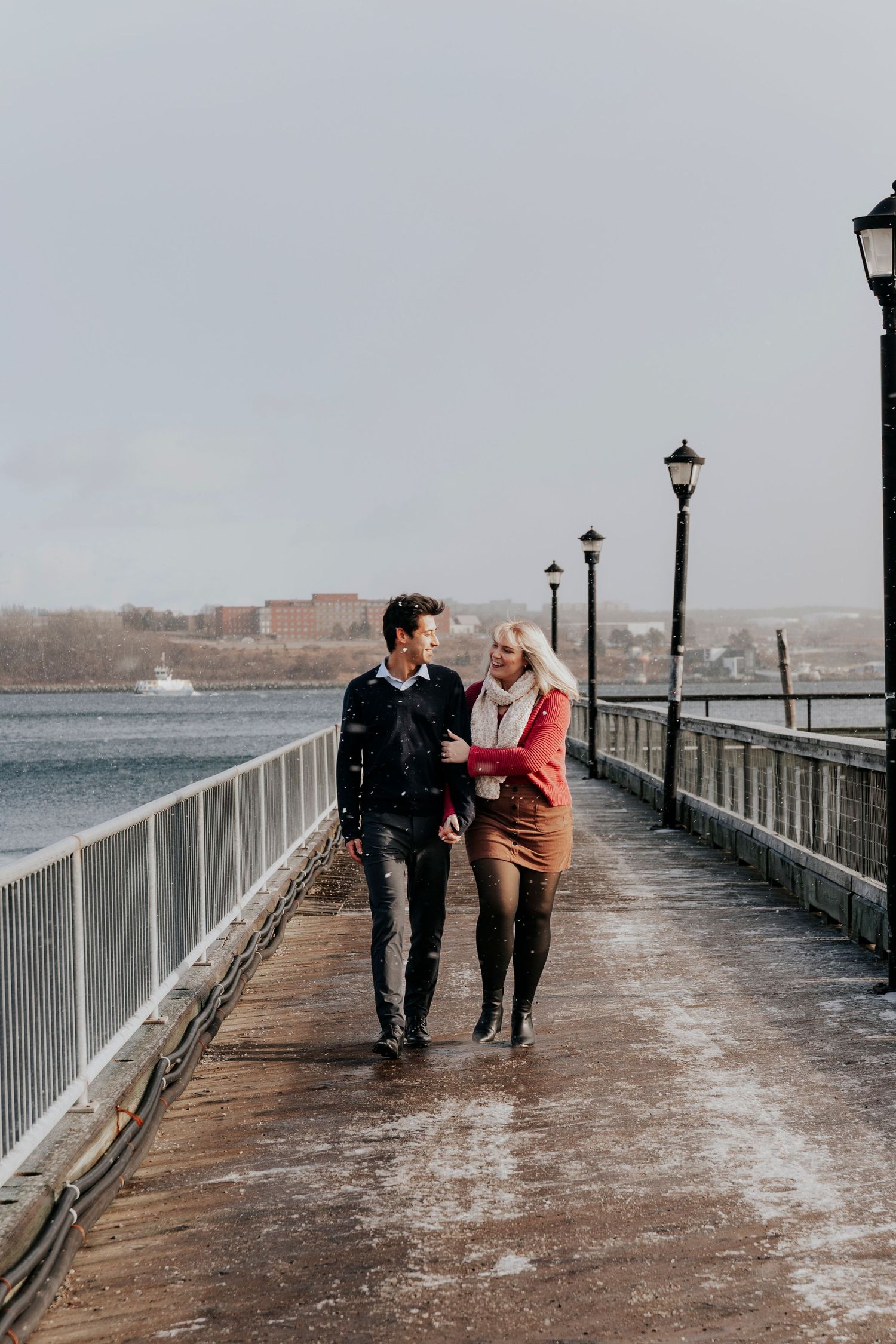Couple walking arm in arm along a waterfront boardwalk on a cloudy winter day.