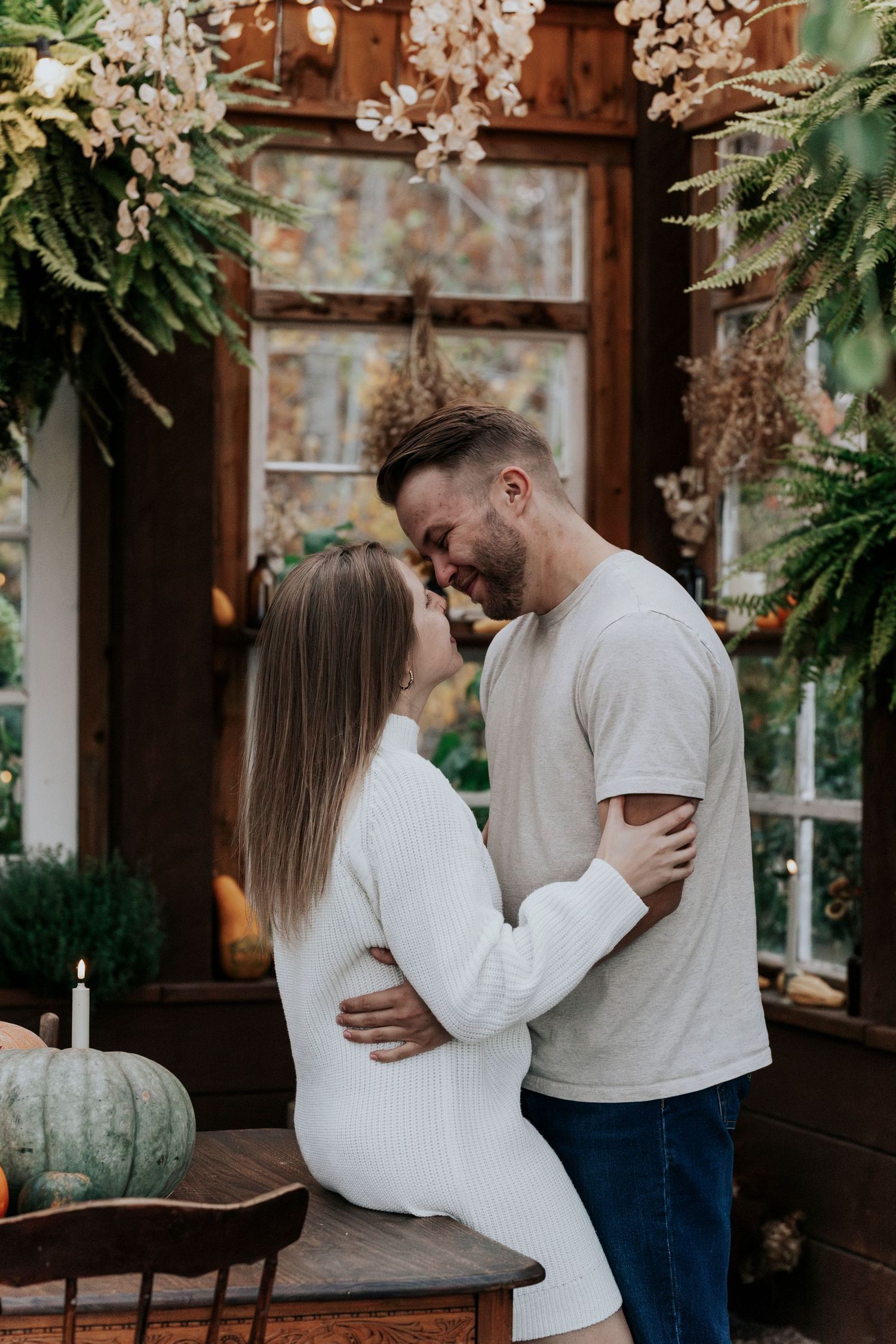 Couple embracing intimately inside a decorated greenhouse with pumpkins and dried botanicals.
