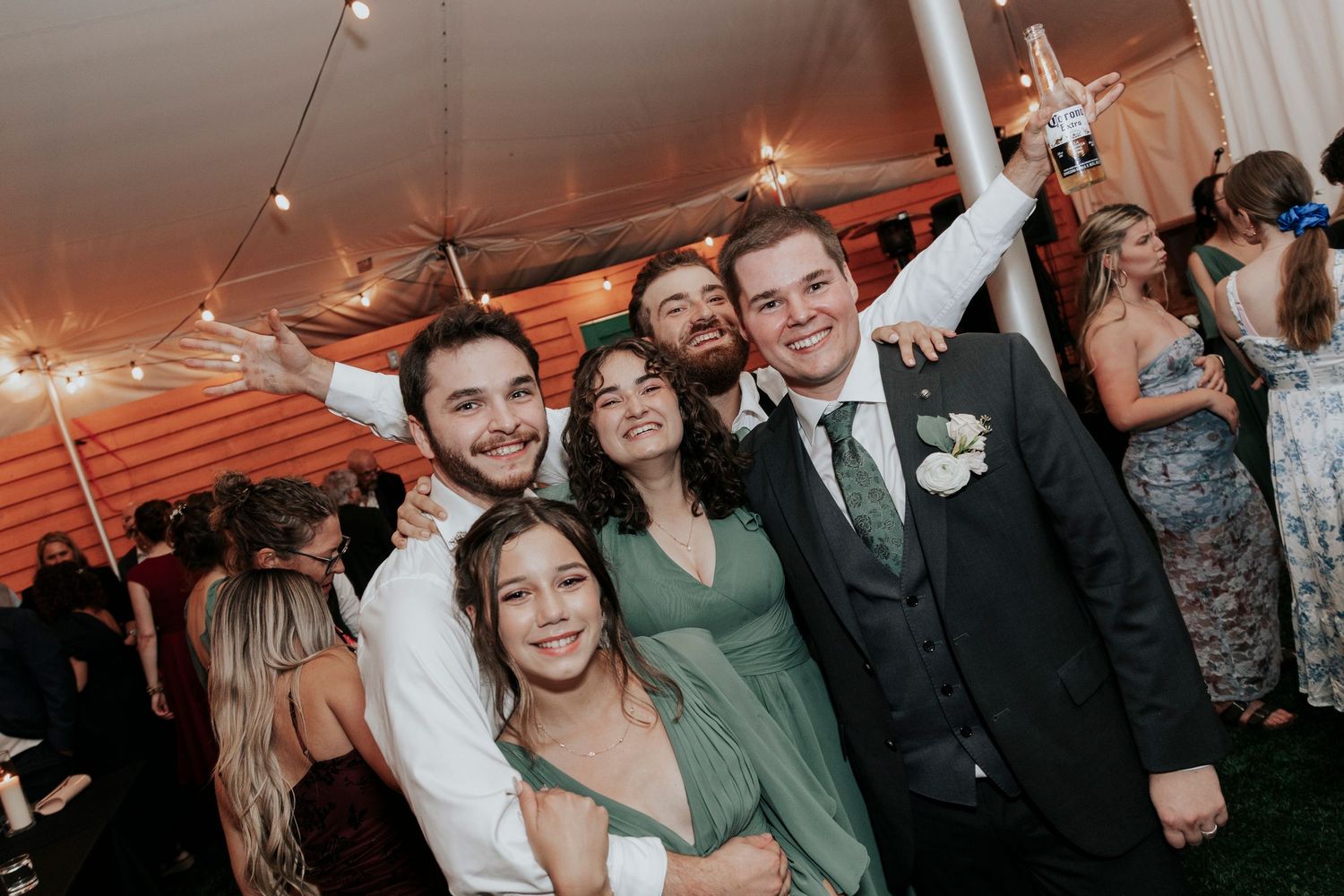 Wedding celebration with group of friends posing joyfully under string lights.