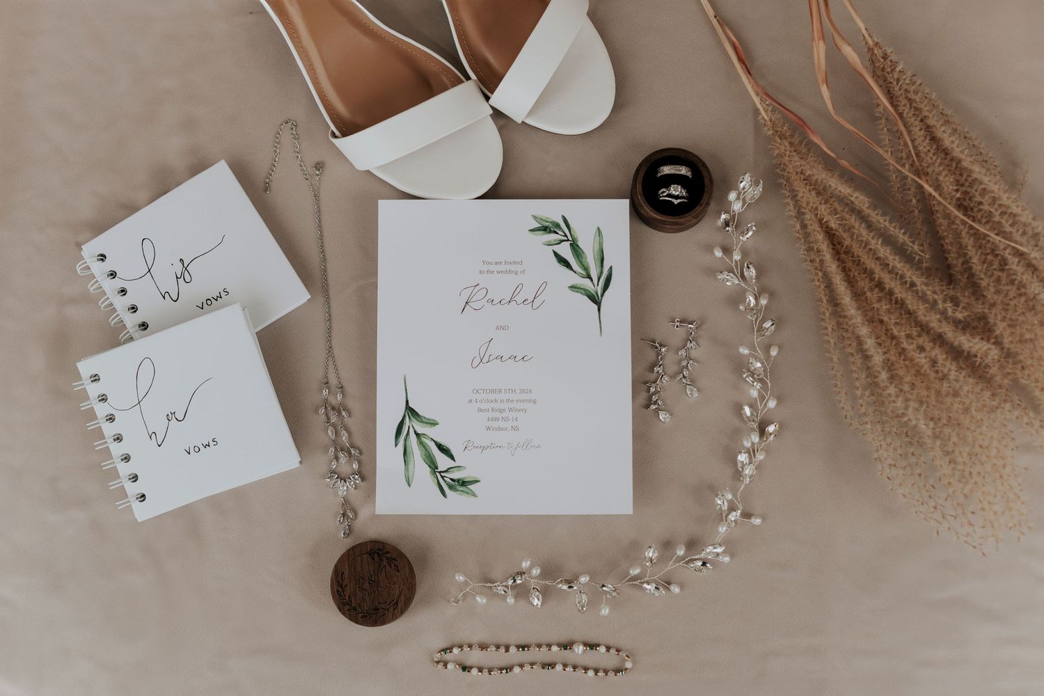 Minimalist wedding invitation with greenery design alongside white heels and dried pampas grass.