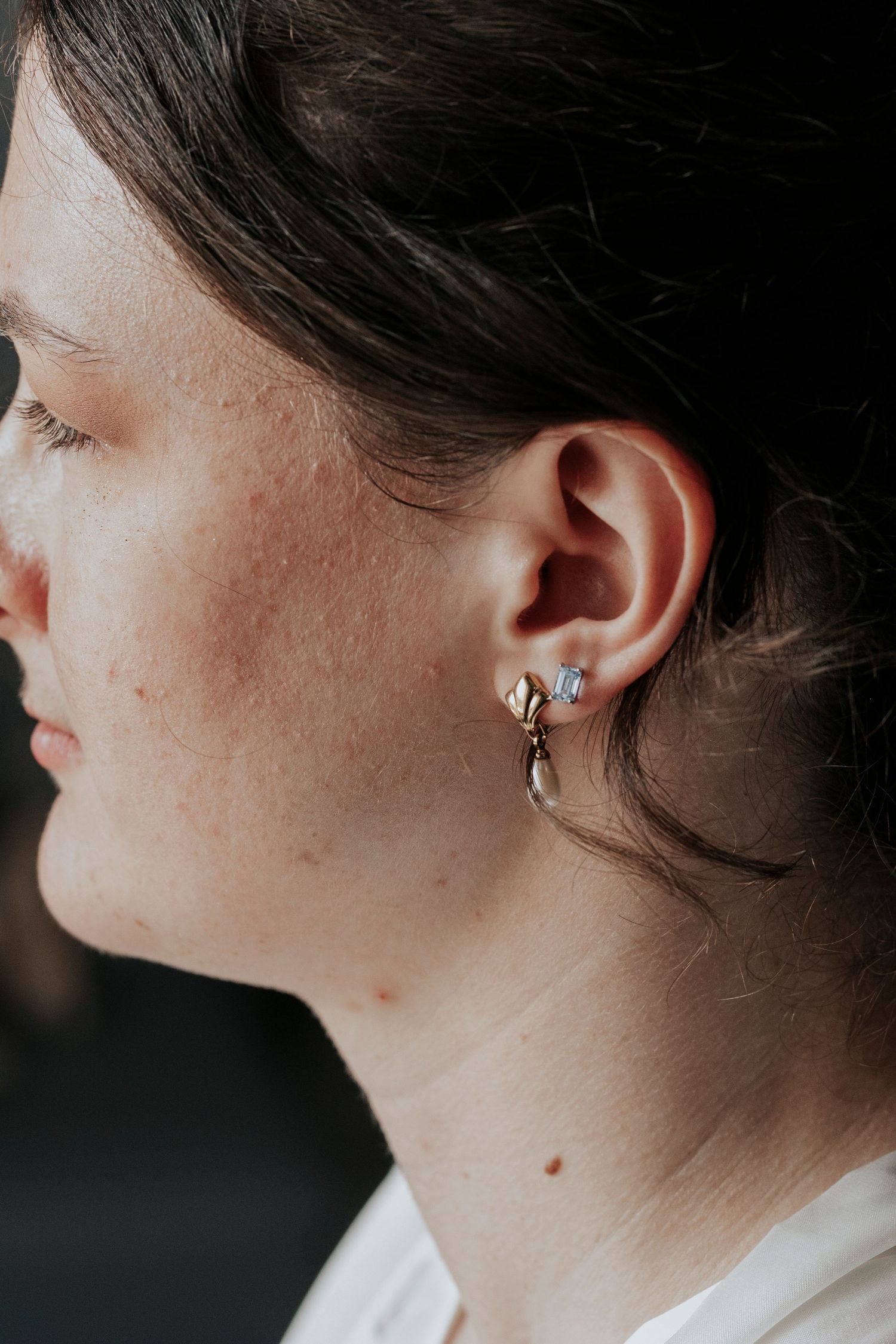 An elegant pearl earring detail shown in profile against a dark background.