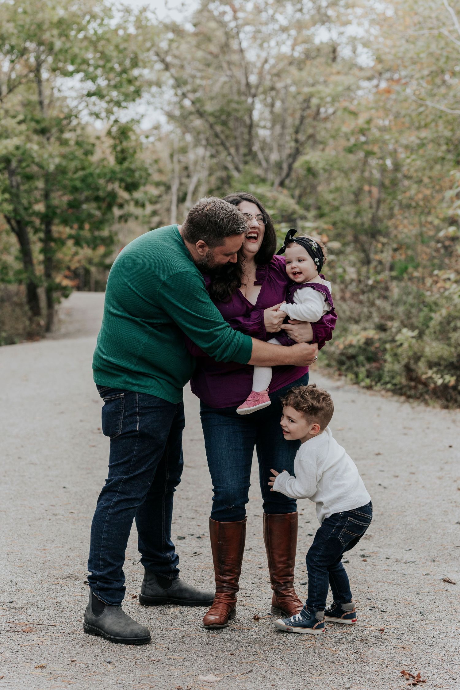 Joyful family of four laughing together on a scenic woodland path in fall.