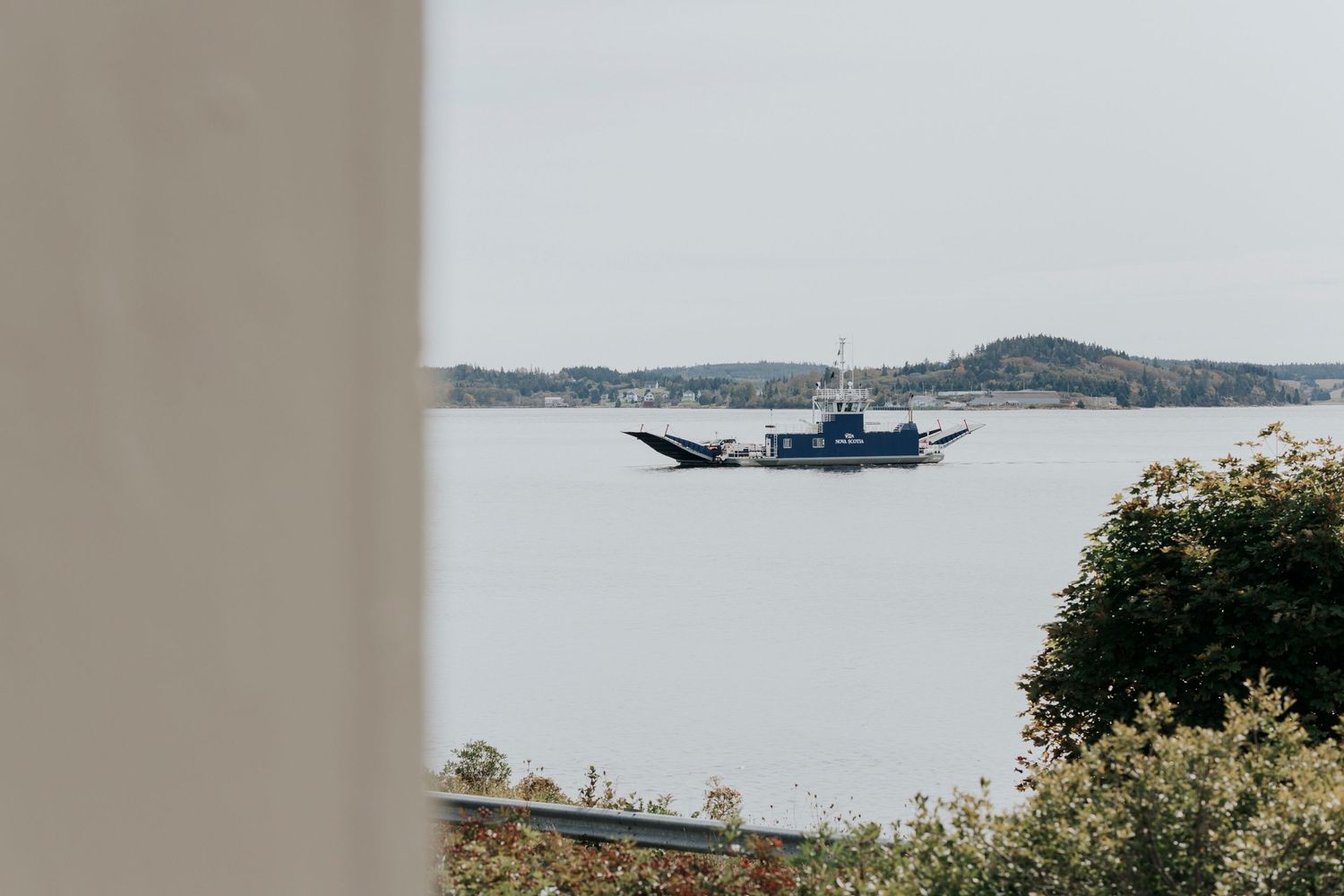 LaHave ferry cruises across calm waters with distant hills and shoreline visible through coastal foliage.