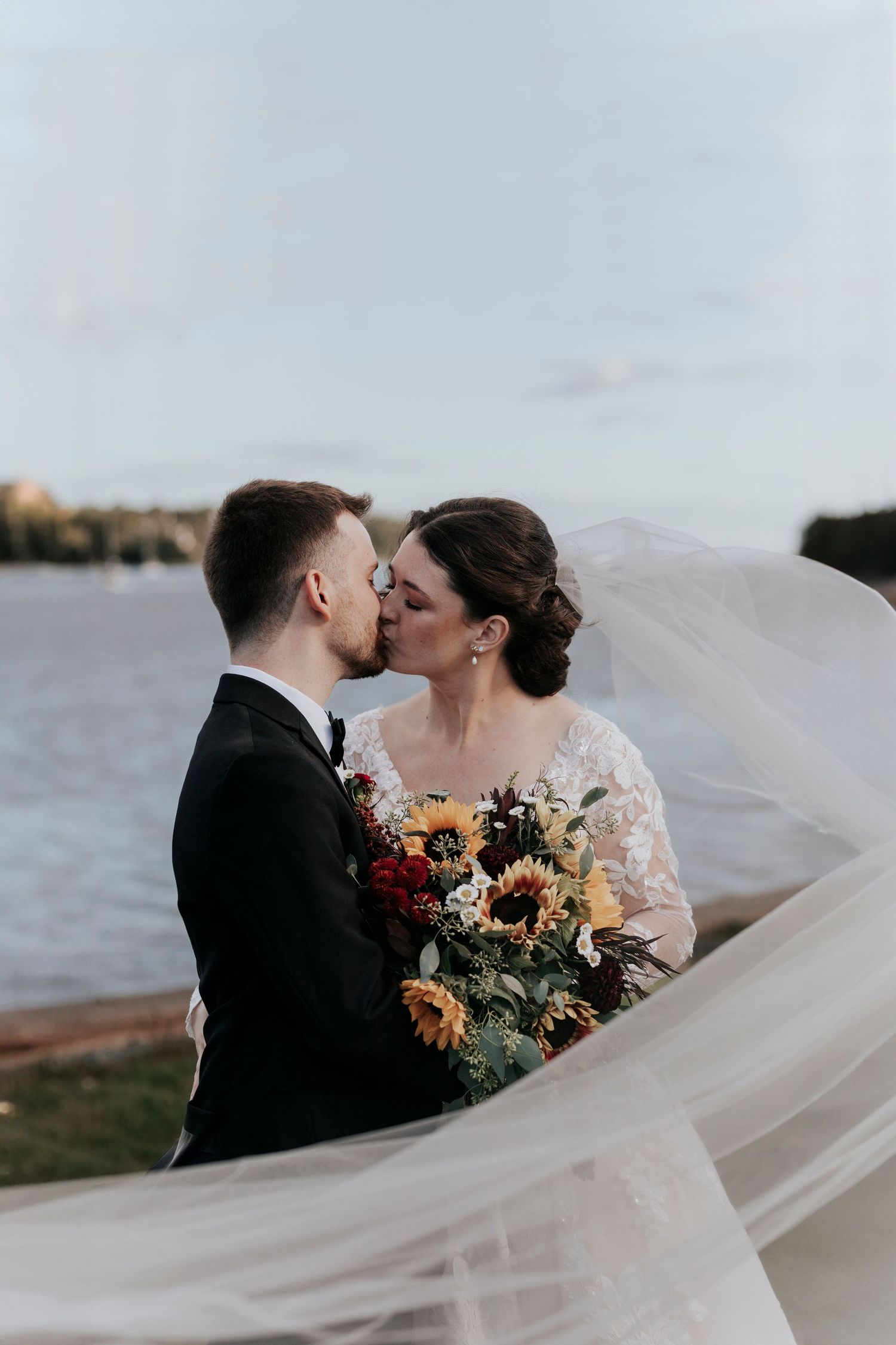 Romantic waterfront wedding portrait with flowing veil and autumn bouquet.