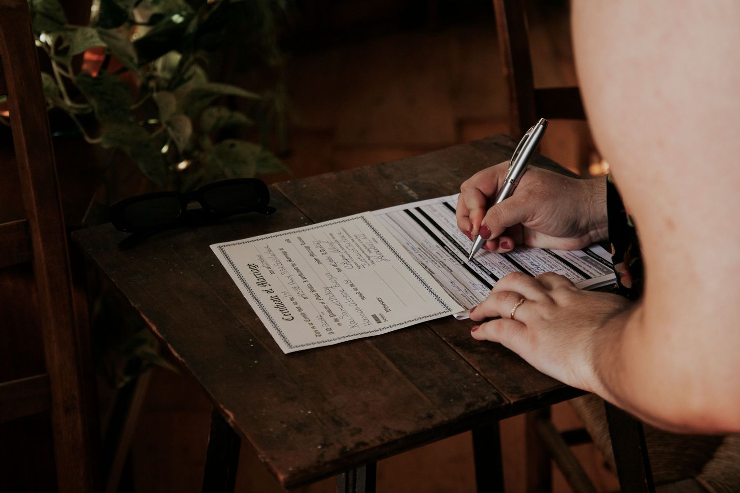 A person's hands fill out legal paperwork using a pen on a dark wooden table.