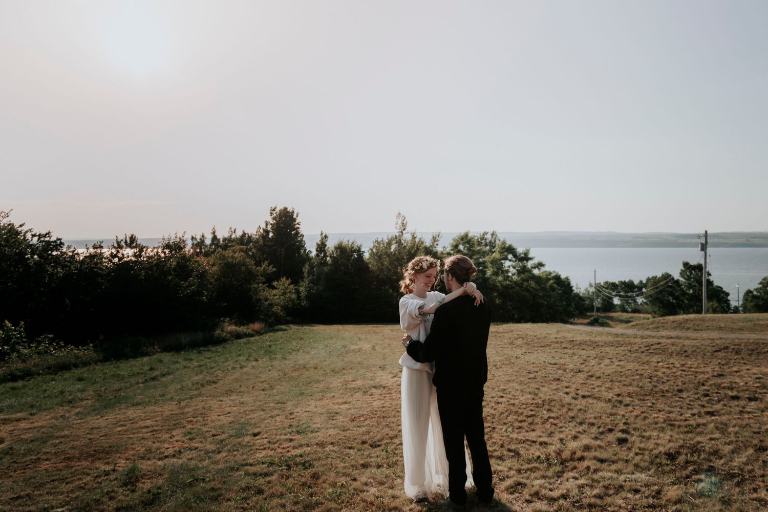 A couple embraces on a grassy cliff overlooking the ocean on an overcast evening.