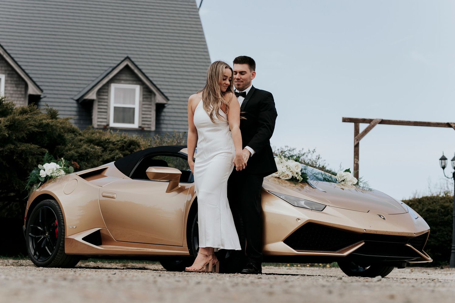 Elegant bride and groom standing together next to a gold Lamborghini convertible outdoors.
