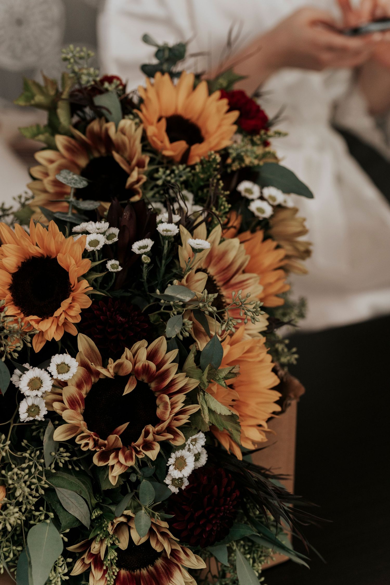 A vibrant wedding bouquet featuring sunflowers, small white blooms, and greenery in rustic autumn style.