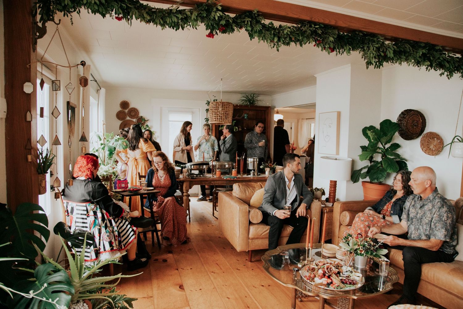 People gather in a warmly-lit room decorated with greenery for a holiday celebration at what appears to be a care facility.