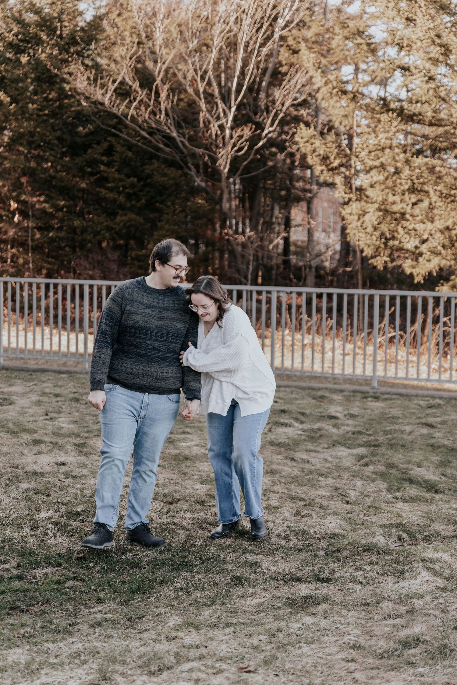 Couple laughing together while walking on a grassy field with autumn trees in background.
