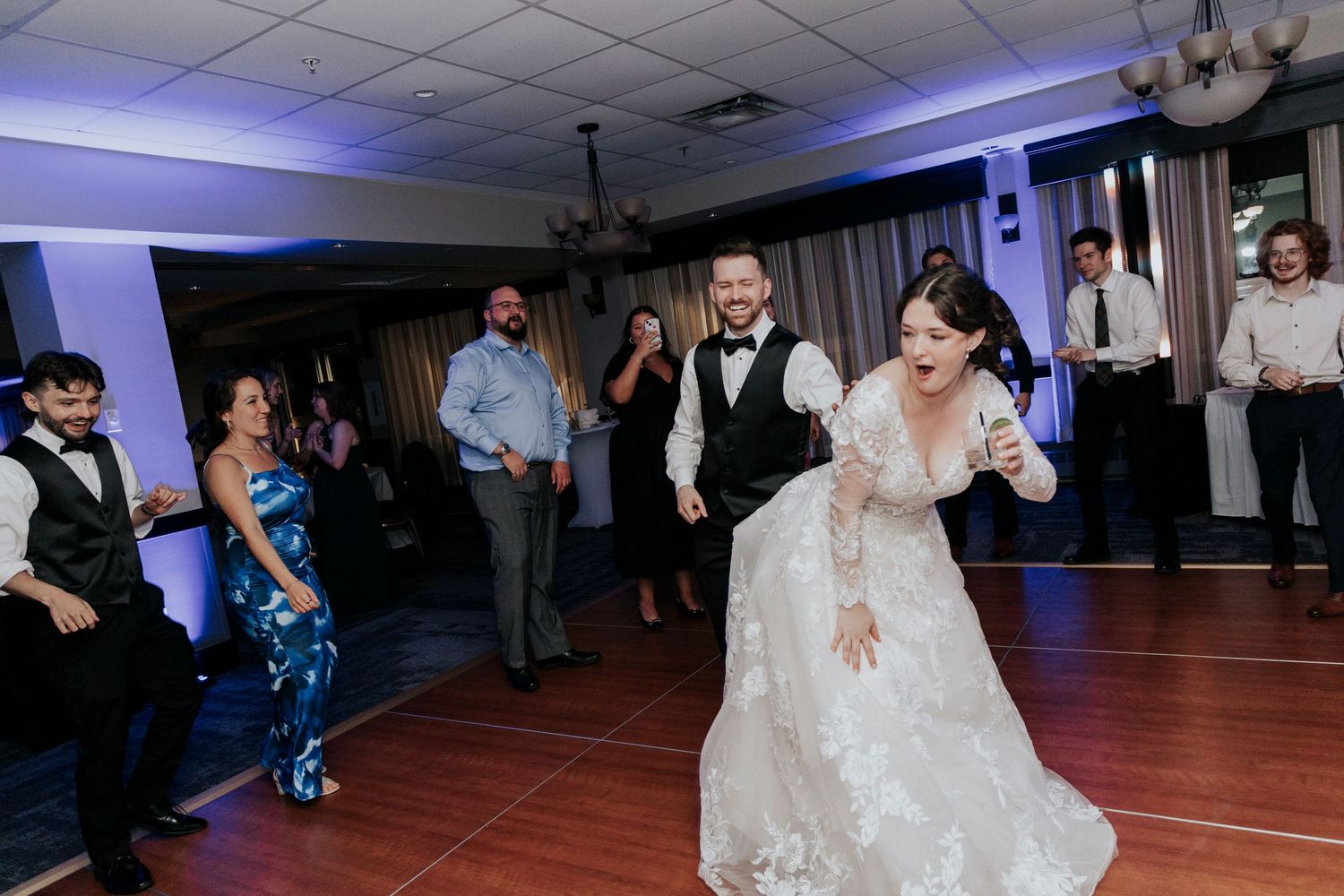 Bride dances energetically on the dance floor surrounded by guests at wedding reception.