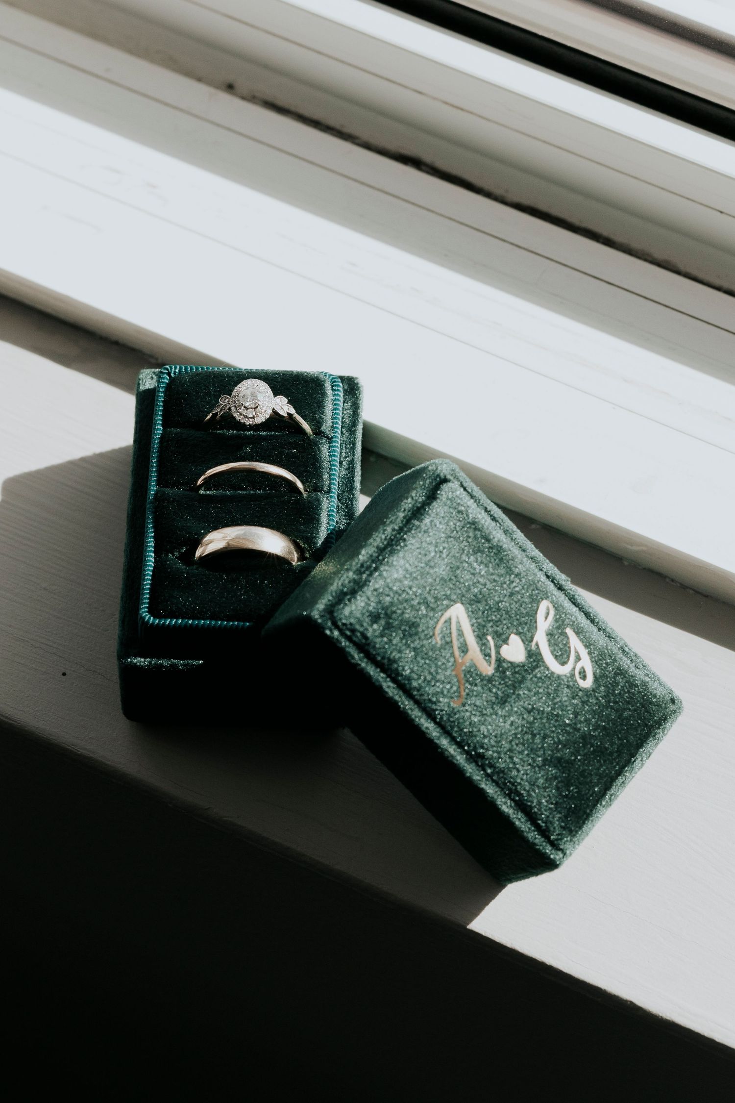 Wedding rings nestled in an emerald green velvet ring box on a windowsill.