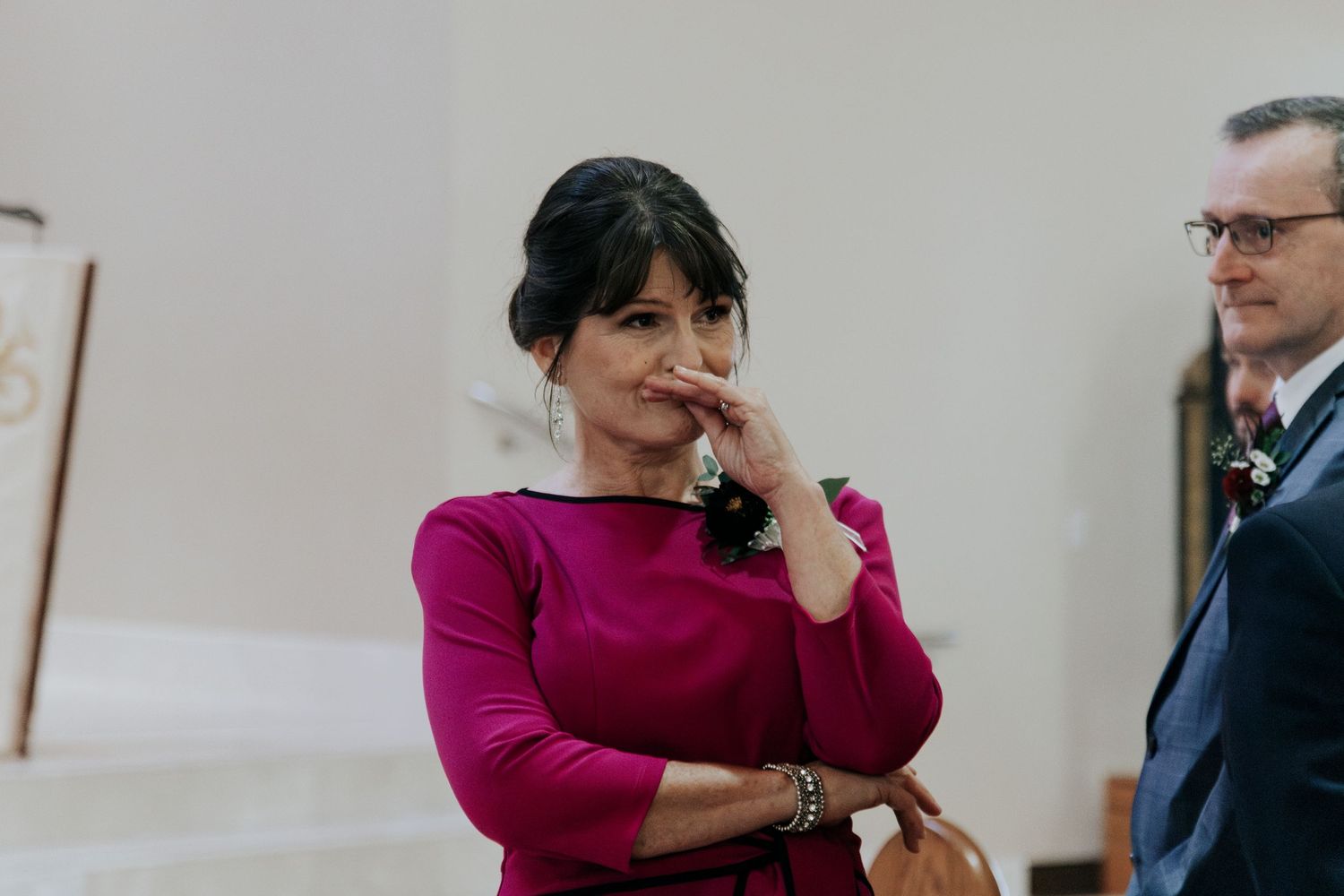 A woman in a magenta dress poses thoughtfully in an elegant church setting.